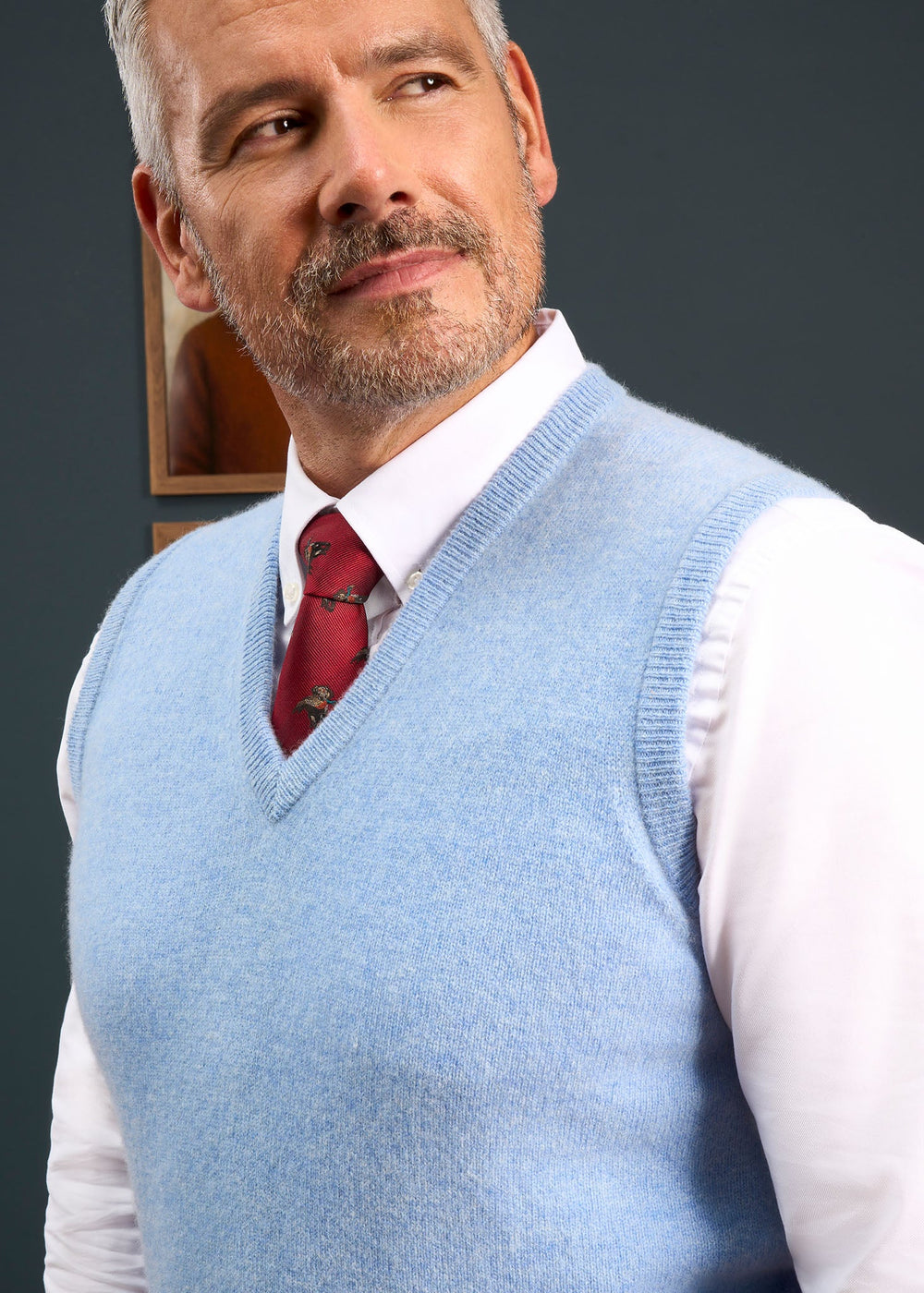 A man wearing a Norfolk Lambswool V-Neck Slipover In Glacier over a white collared shirt and red tie.