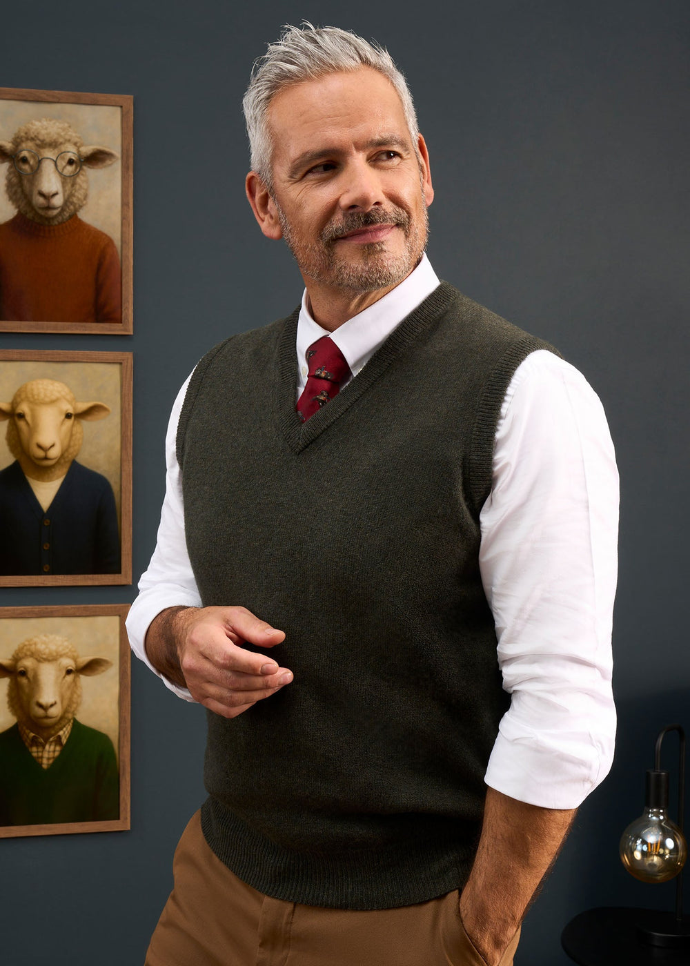 A man wears a dark green Norfolk Lambswool V-Neck Slipover In Seaweed over a white shirt and red tie.