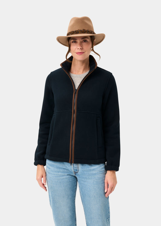 Woman in jeans and tan hat wears the Aylsham Ladies Fleece Jacket in Dark Navy, standing before a plain white background.
