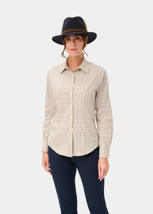 Woman in Bromford Ladies Cotton Shirt in Red Check, navy feathered hat, and dark pants stands by a plain light background.
