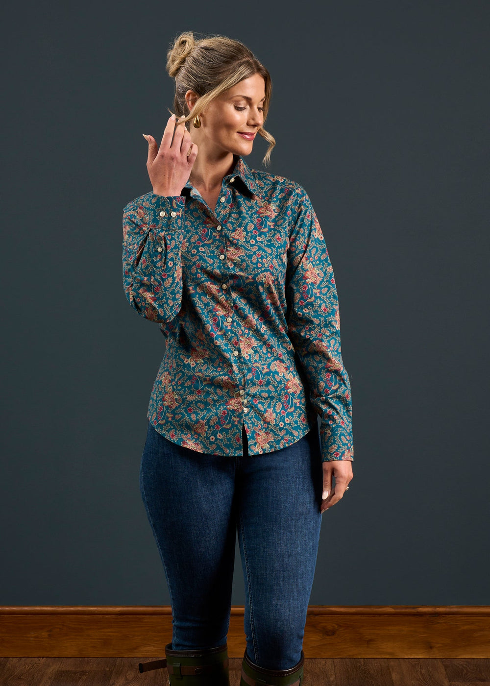 Woman in Lawen Cotton Printed Shirt in Blue Floral, regular fit, with jeans, smiles and brushes hair back on wooden floor.