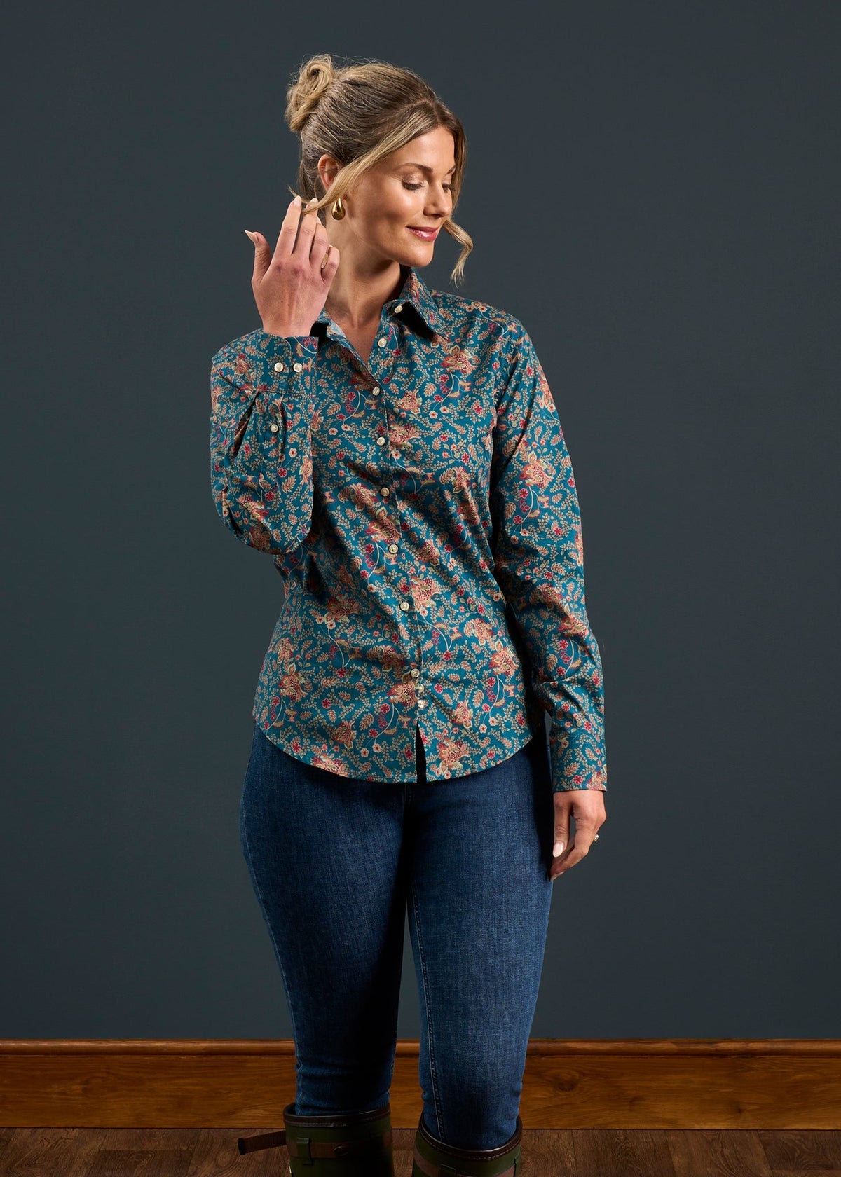 Woman in Lawen Cotton Printed Shirt in Blue Floral, regular fit, with jeans, smiles and brushes hair back on wooden floor.