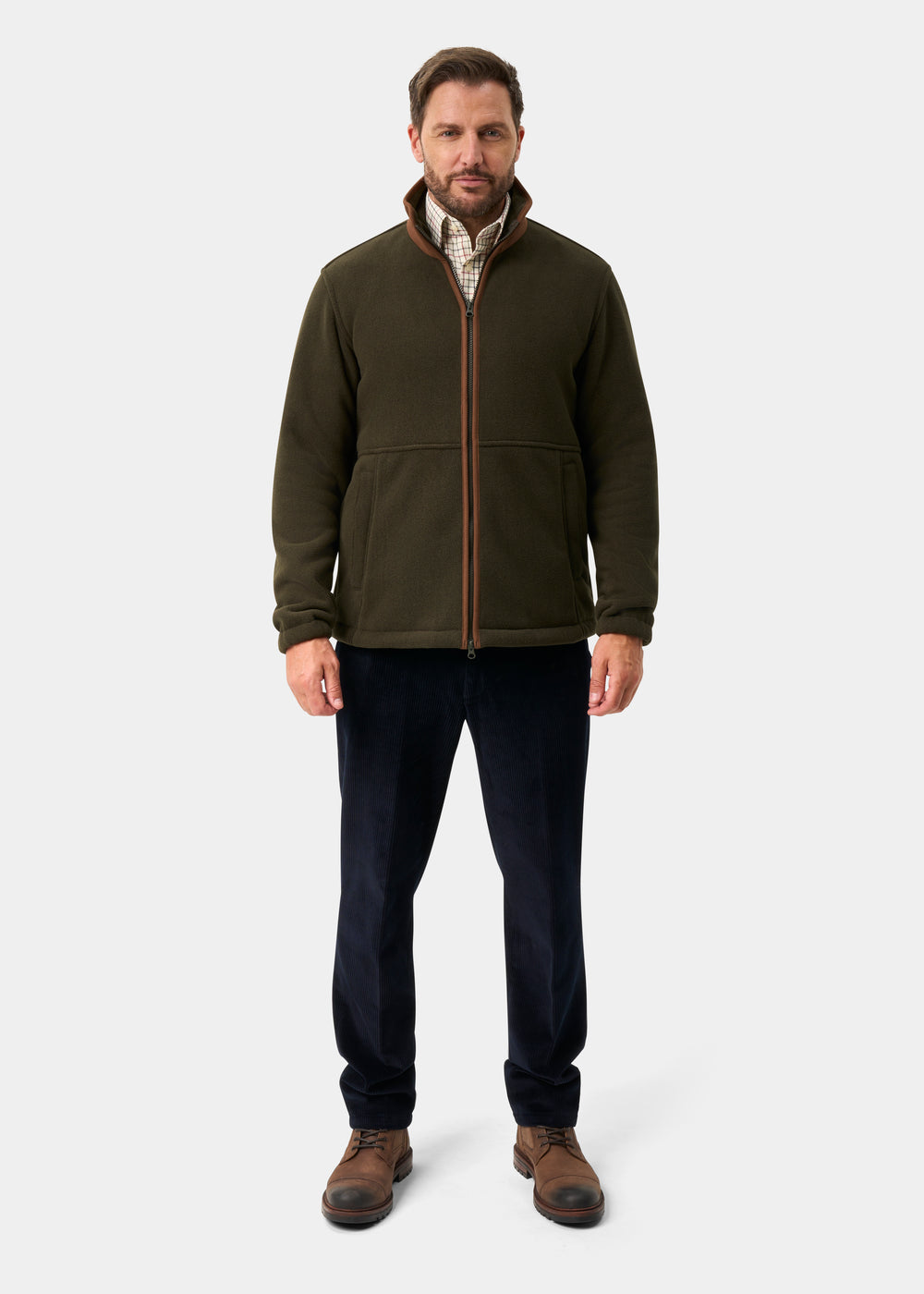 Man wears Aylsham Men’s Fleece Jacket in green, plaid shirt, dark pants, and brown boots against a plain background.
