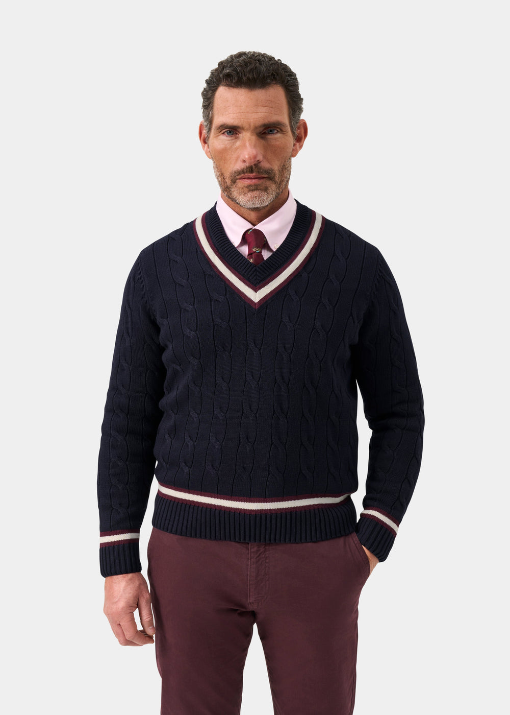 A man wears a Sandridge Cotton Cable Knit V-Neck Cricket Jumper in dark navy and blackcurrant over a pink shirt and a tie.