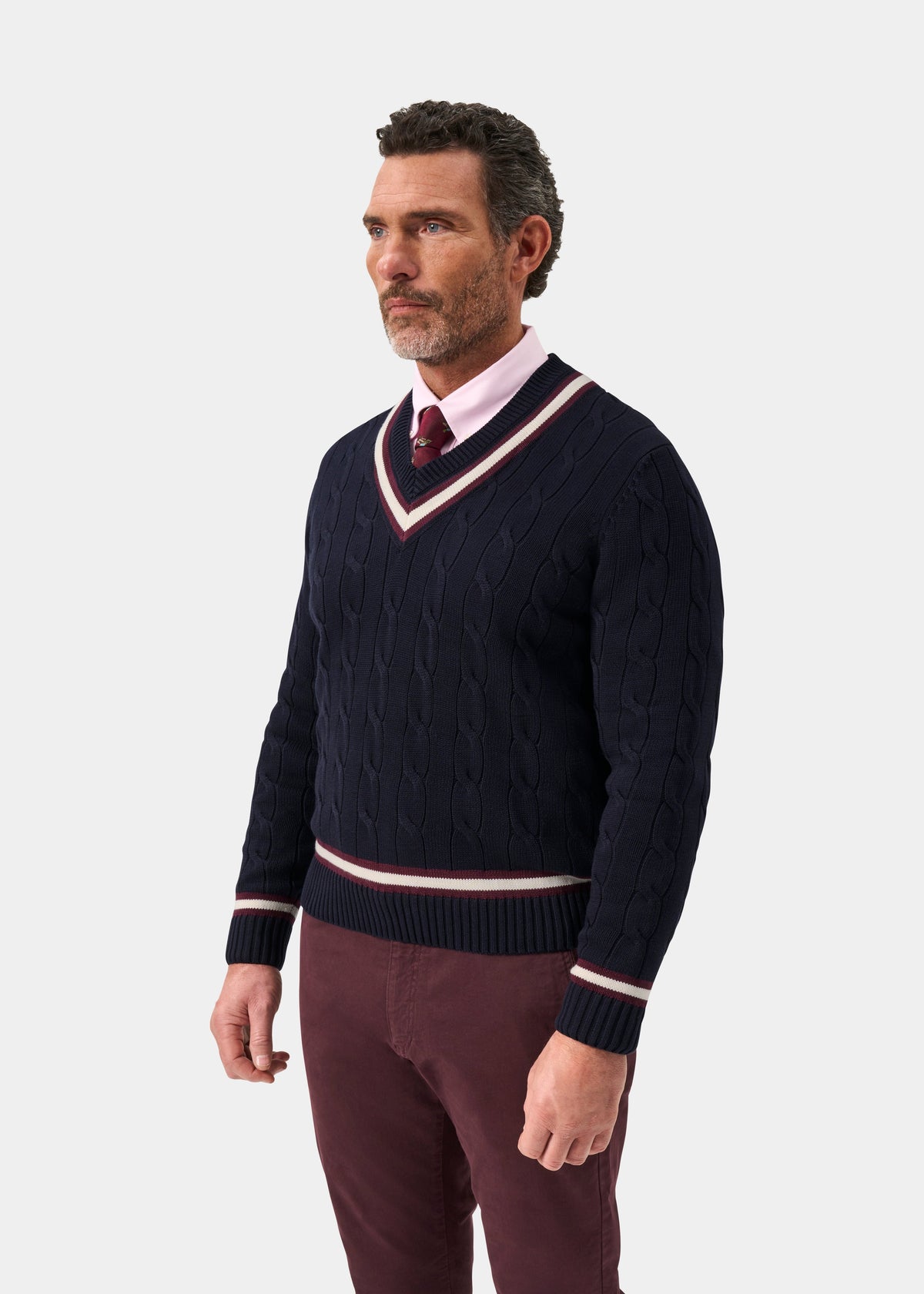 Man wearing a Sandridge Cotton Cable Knit V-Neck Cricket Jumper In Dark Navy and Blackcurrant over a pink shirt.