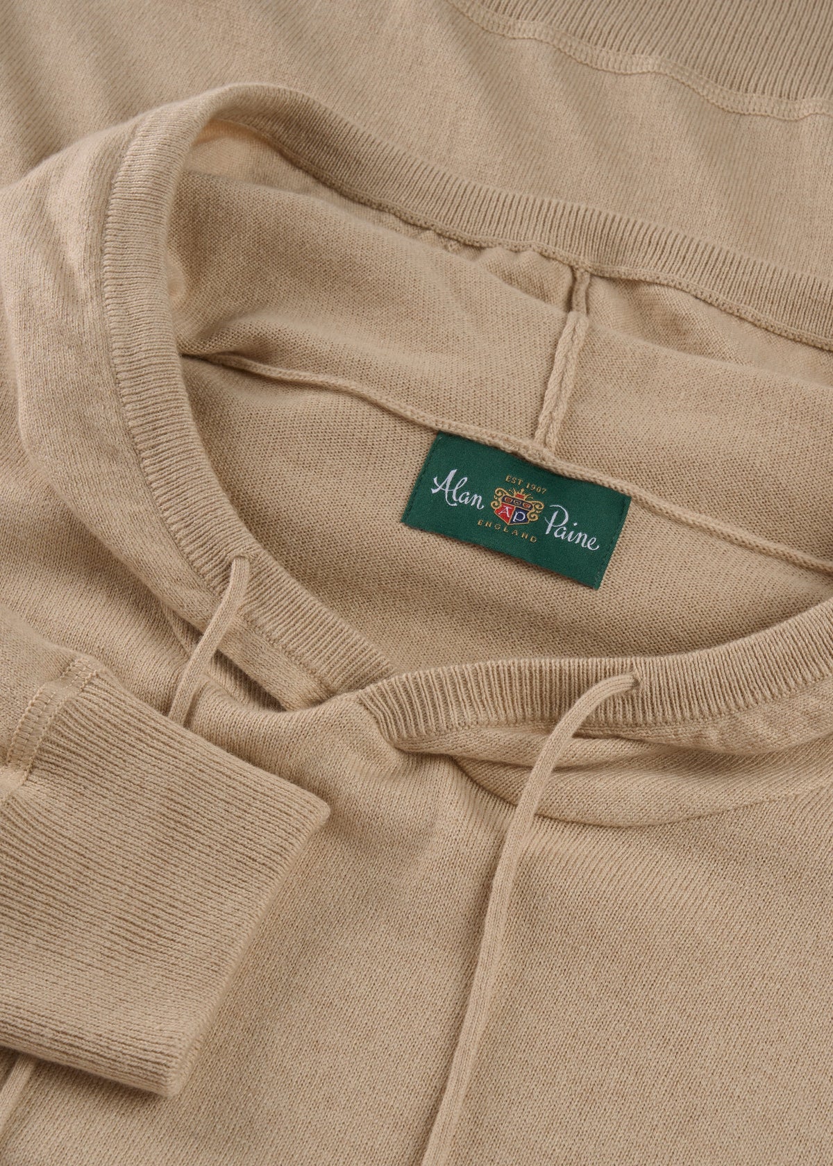 Close-up of the Gaisby Cotton Merino Hoodie in Oatmeal, showing hood, drawstrings, and green Alan Paine neck label.