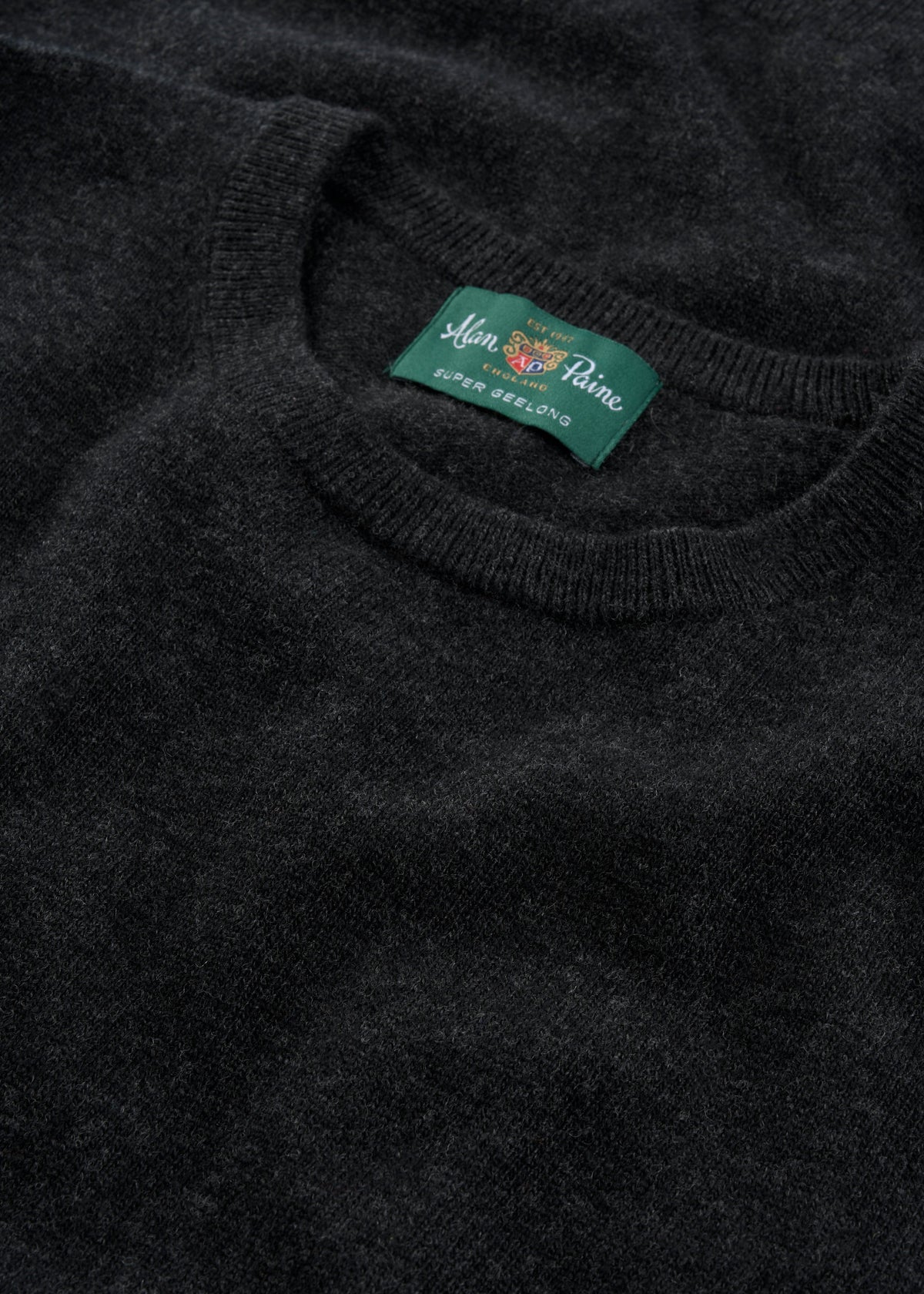 Close-up of the Brisbane Geelong Wool Crew Neck Jumper in Charcoal - Regular Fit, featuring a green Super Geelong label.