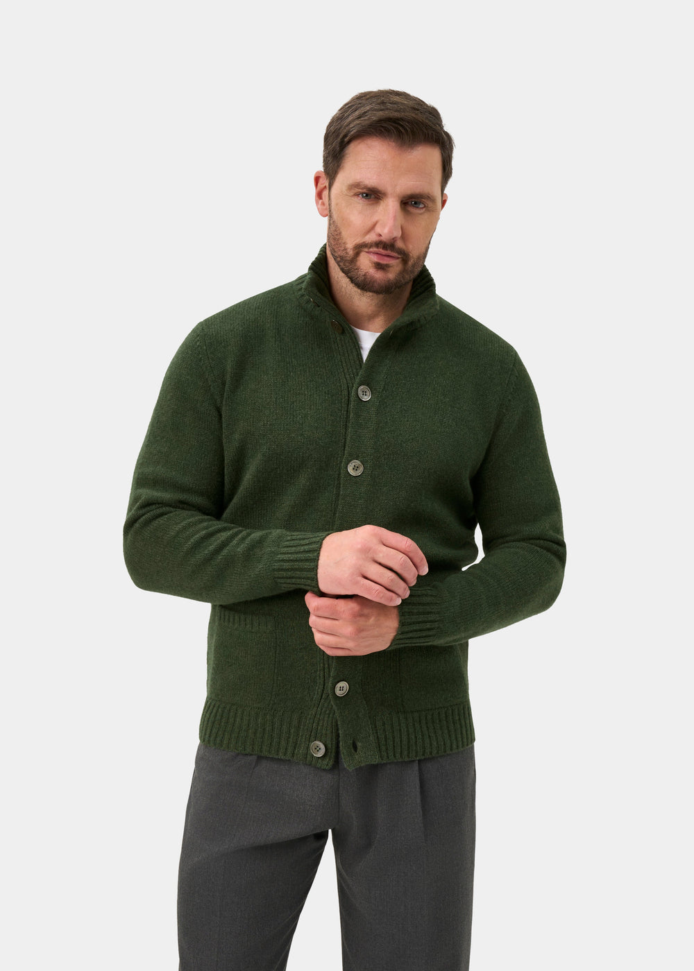 Man wears Landford Lambswool Buttoned Mock Neck Jumper in Rosemary and gray pants against a plain white background.