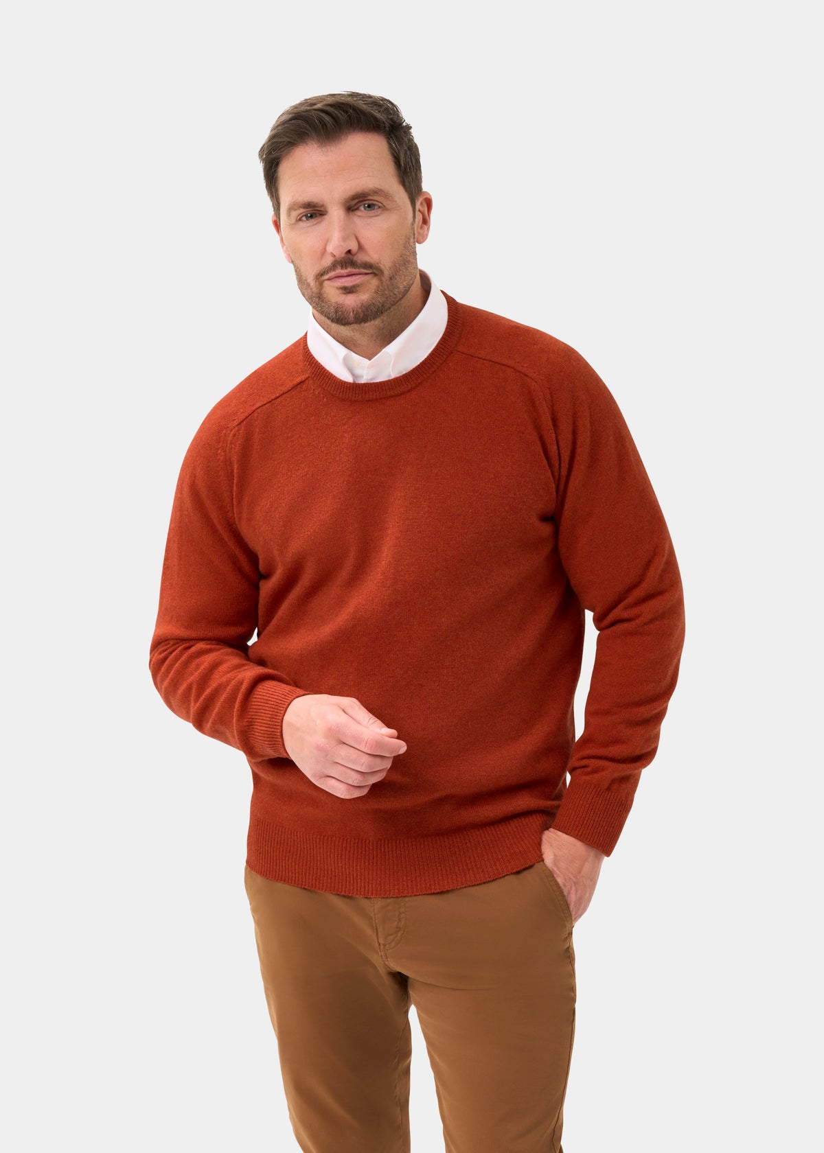 Man in Dorset Lambswool Crew Neck Jumper in Ember and brown pants stands against a white background, facing the camera.