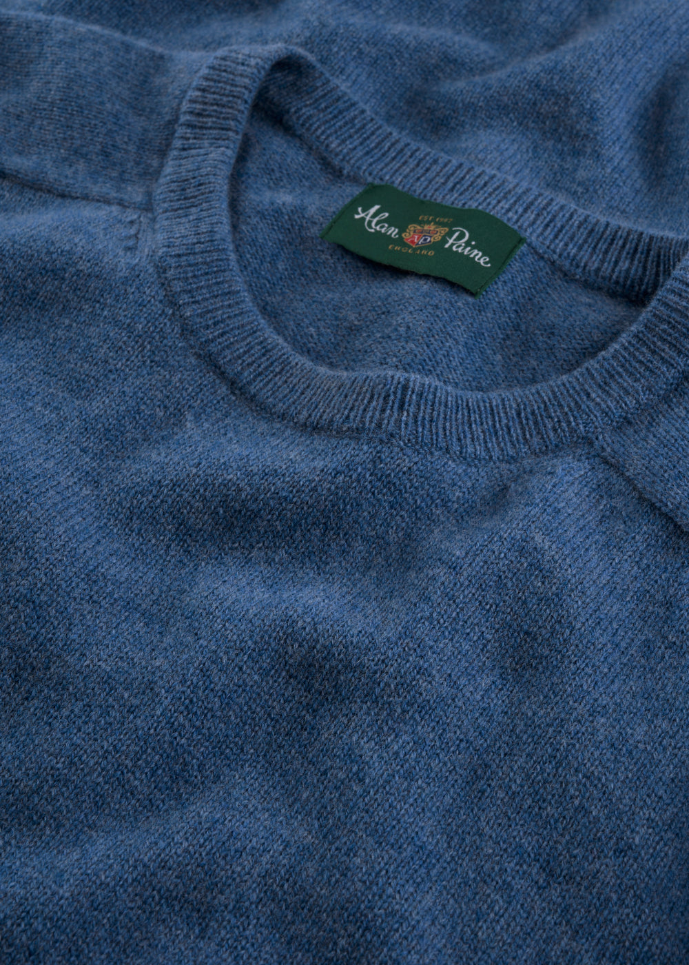 Close-up of the Lenzie Lambswool Crew Neck Jumper in Jeans with a green Alan Paine label at the neckline.
