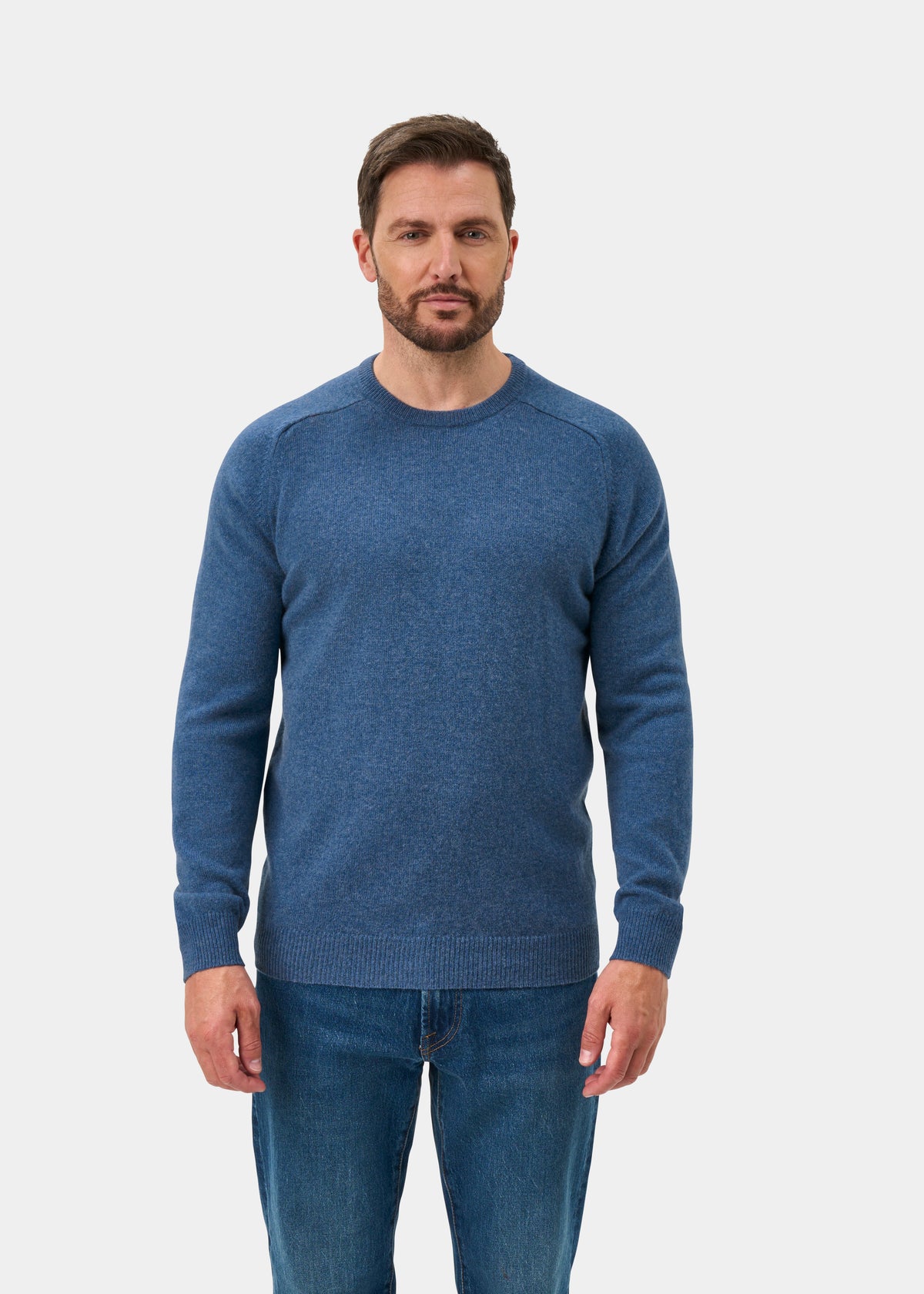 Man with short brown hair models the Lenzie Lambswool Crew Neck Jumper In Jeans - Regular Fit against a white backdrop.