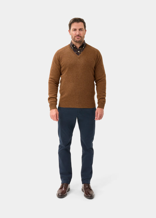 Man in a Hampshire Lambswool Vee Neck Jumper (Driftwood), dark pants, brown shoes, on a white background.