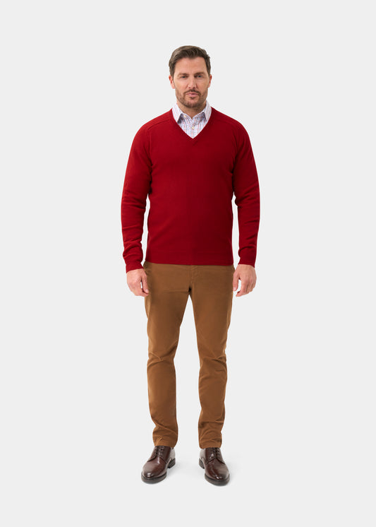 Man in a Dubonnet Hampshire Lambswool Vee Neck Jumper, brown pants, and shoes stands against a white background.