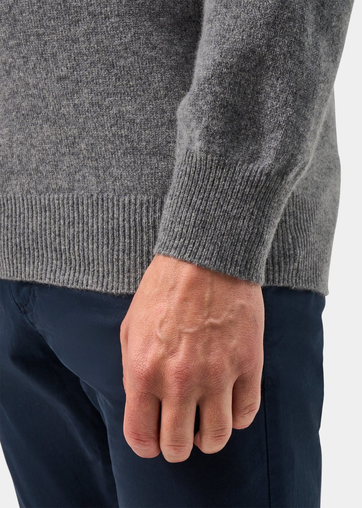 A person wears the Hampshire Lambswool V-Neck Jumper in Grey Mix, paired with dark blue pants, waist-down view.