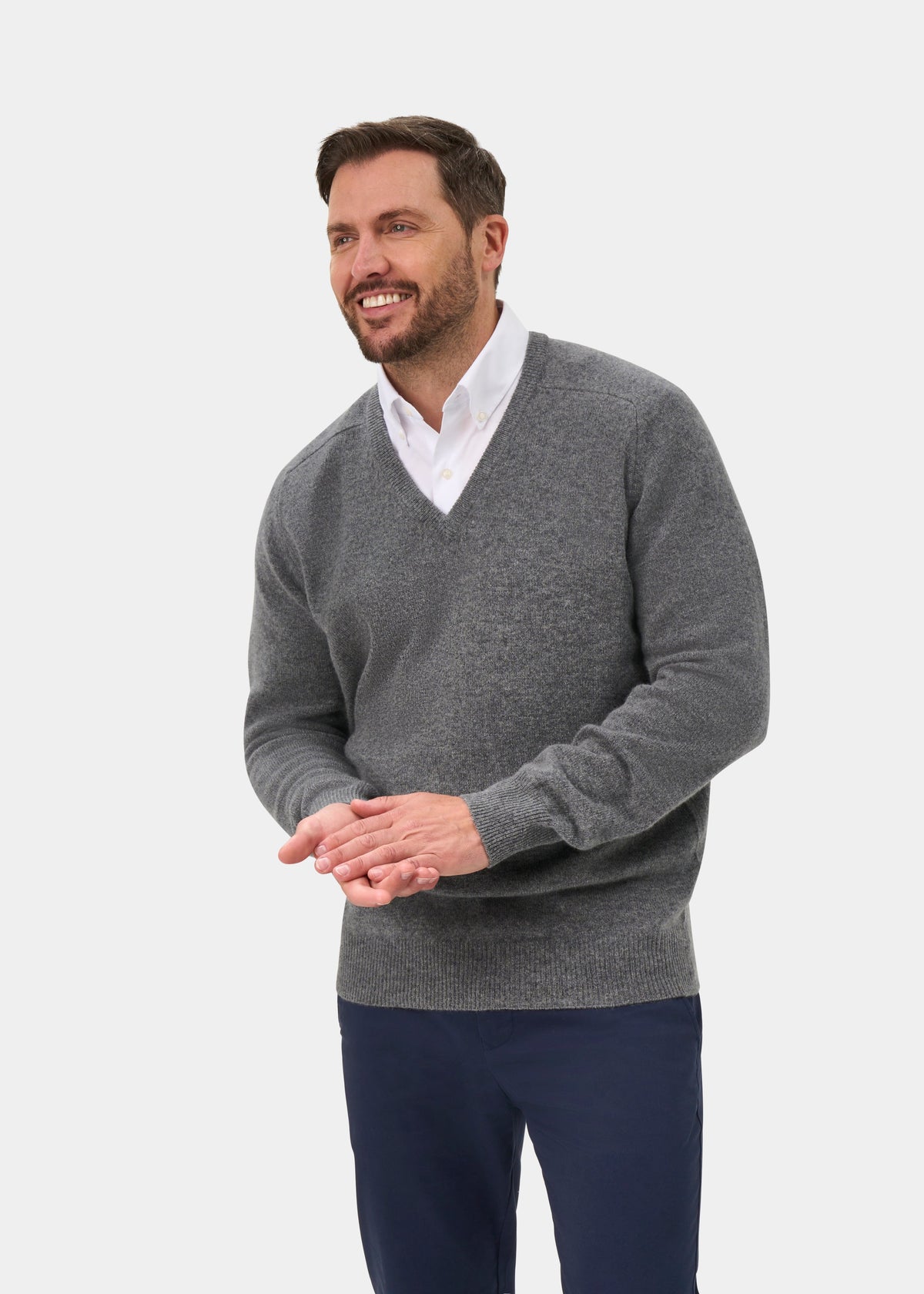 Smiling man models the Hampshire Lambswool V-Neck Jumper in Grey Mix, classic fit, over a white shirt and navy pants.