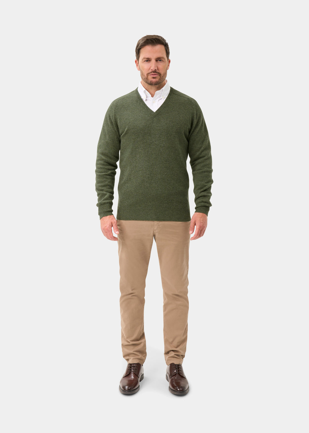 Man in Hampshire Lambswool V-Neck Jumper in Landscape, khaki pants, white shirt, brown shoes; plain light background.