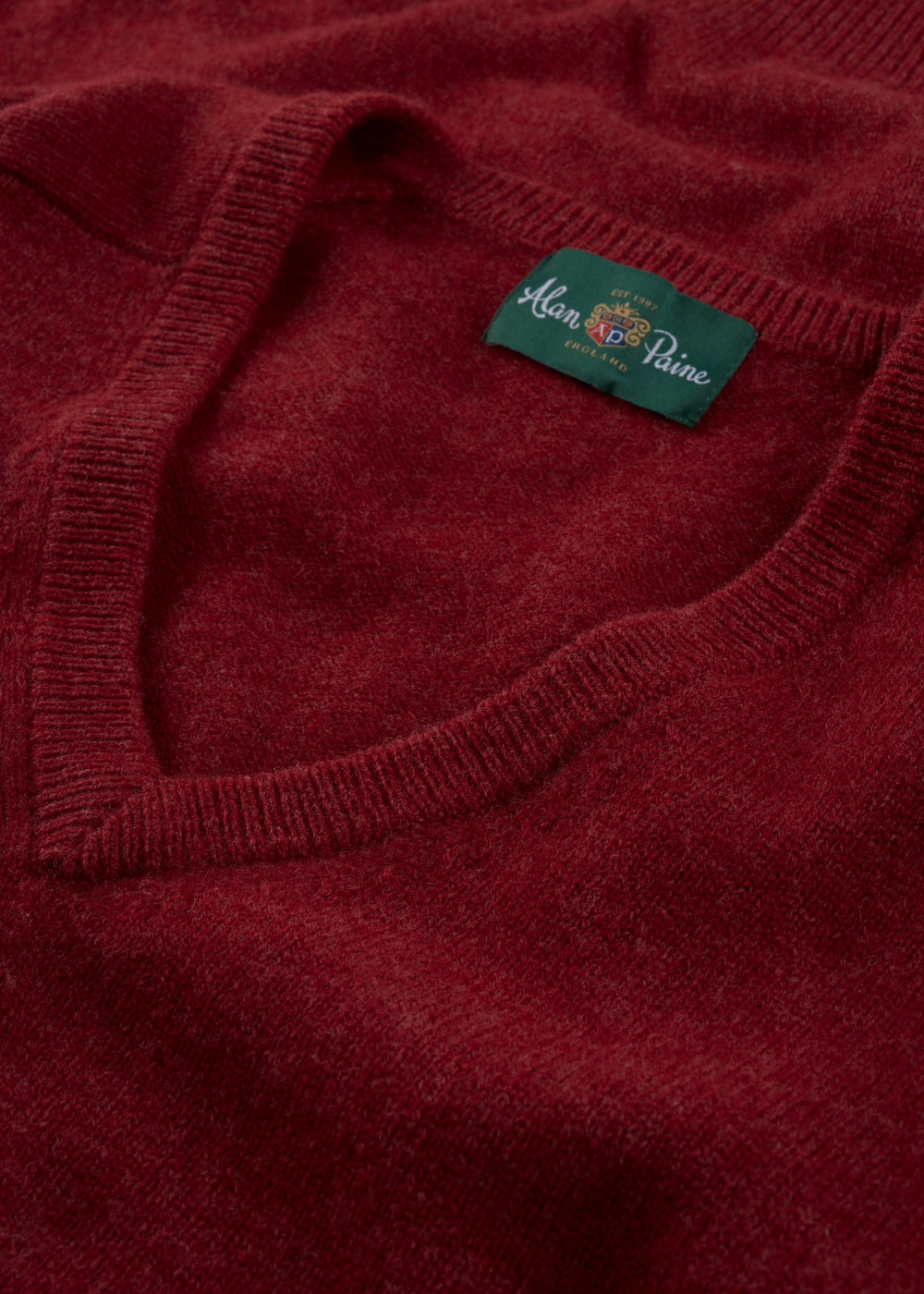 Close-up of a red Hampshire Lambswool Vee Neck Jumper in Poppy, classic fit, with green Alan Paine label at collar.