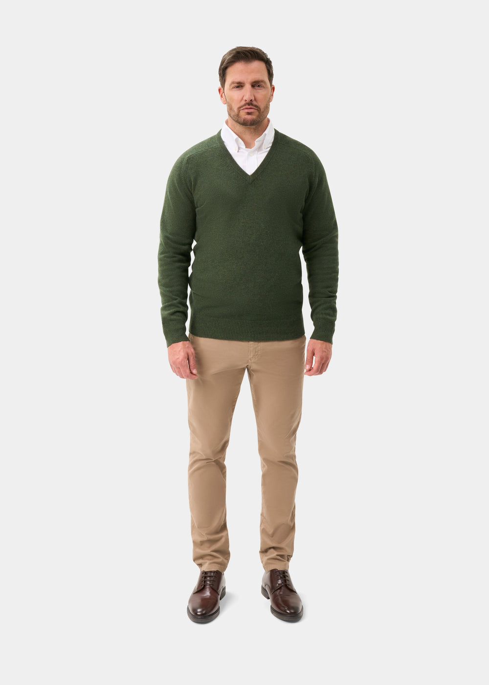 Man in Hampshire Lambswool V-Neck Jumper in Rosemary, white shirt, beige pants, brown shoes on white background.