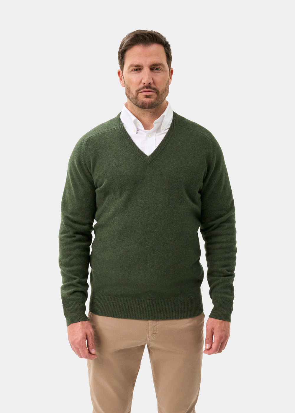 Man in Hampshire Lambswool V-Neck Jumper in Rosemary over a white shirt, beige pants, against a light background.