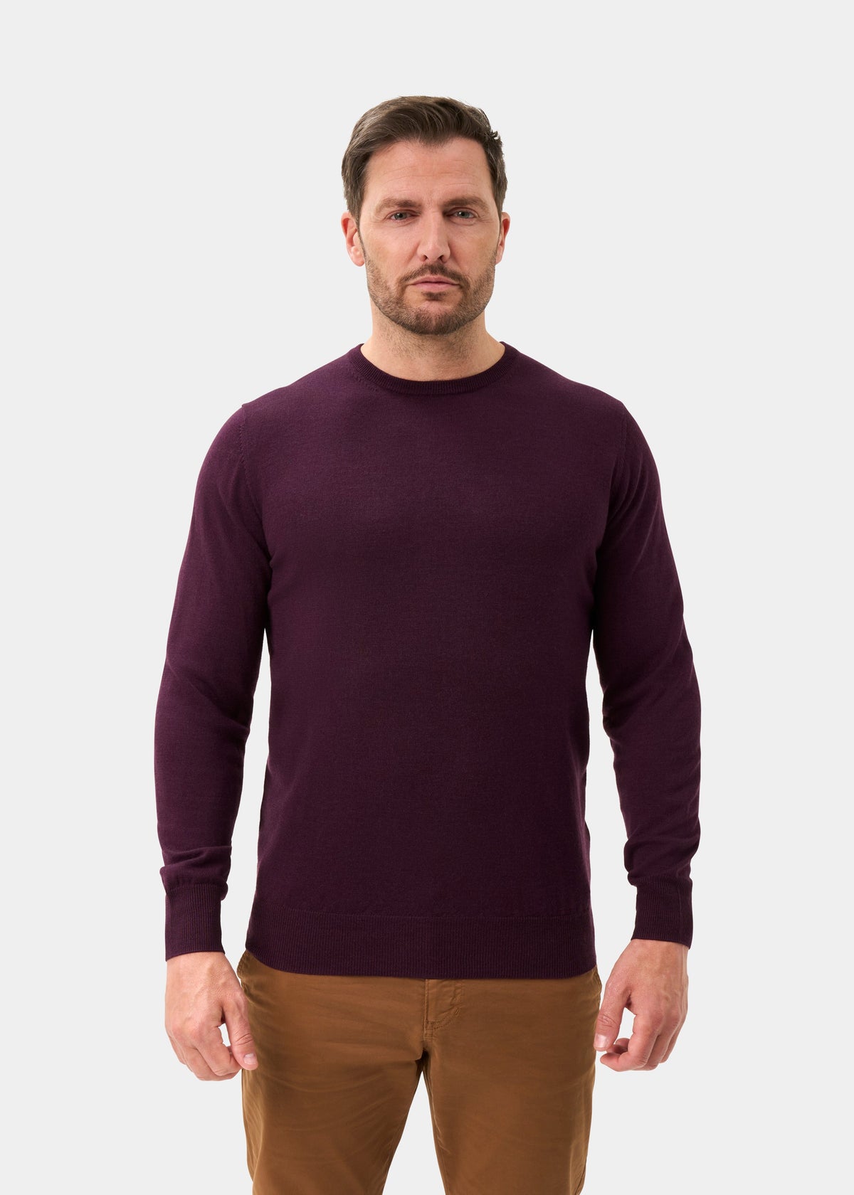 A man wearing a Radstone Merino Wool Crew Neck Jumper In Black Grape and brown trousers.