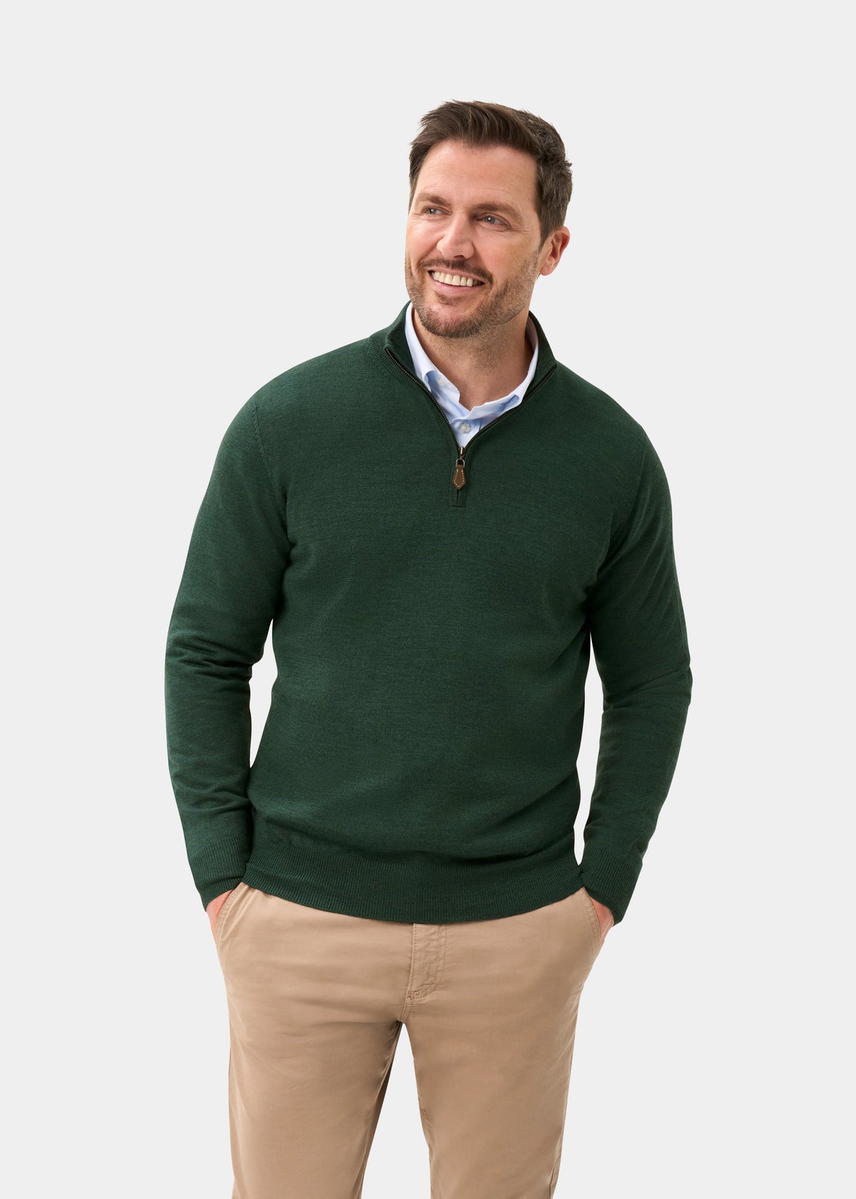 Smiling man wears Barton Merino Wool Quarter Zip Jumper in Hunter and khaki pants, hands in pockets, plain background.