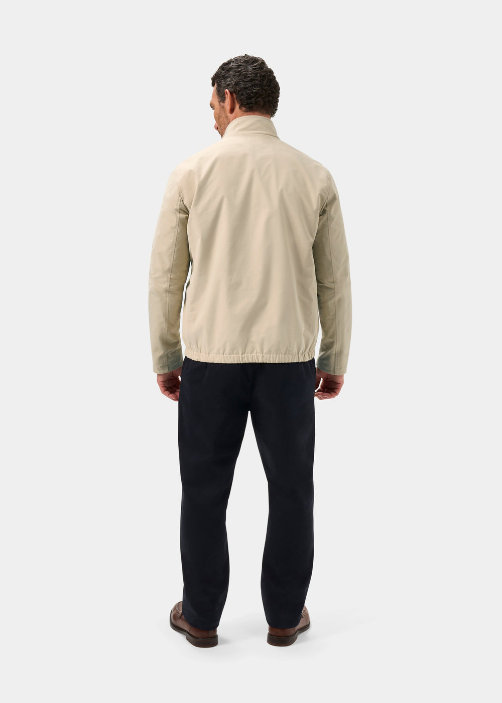 Man facing away in Lakeward Men’s Reversible Bomber Jacket (beige), dark pants, brown shoes, on white background.