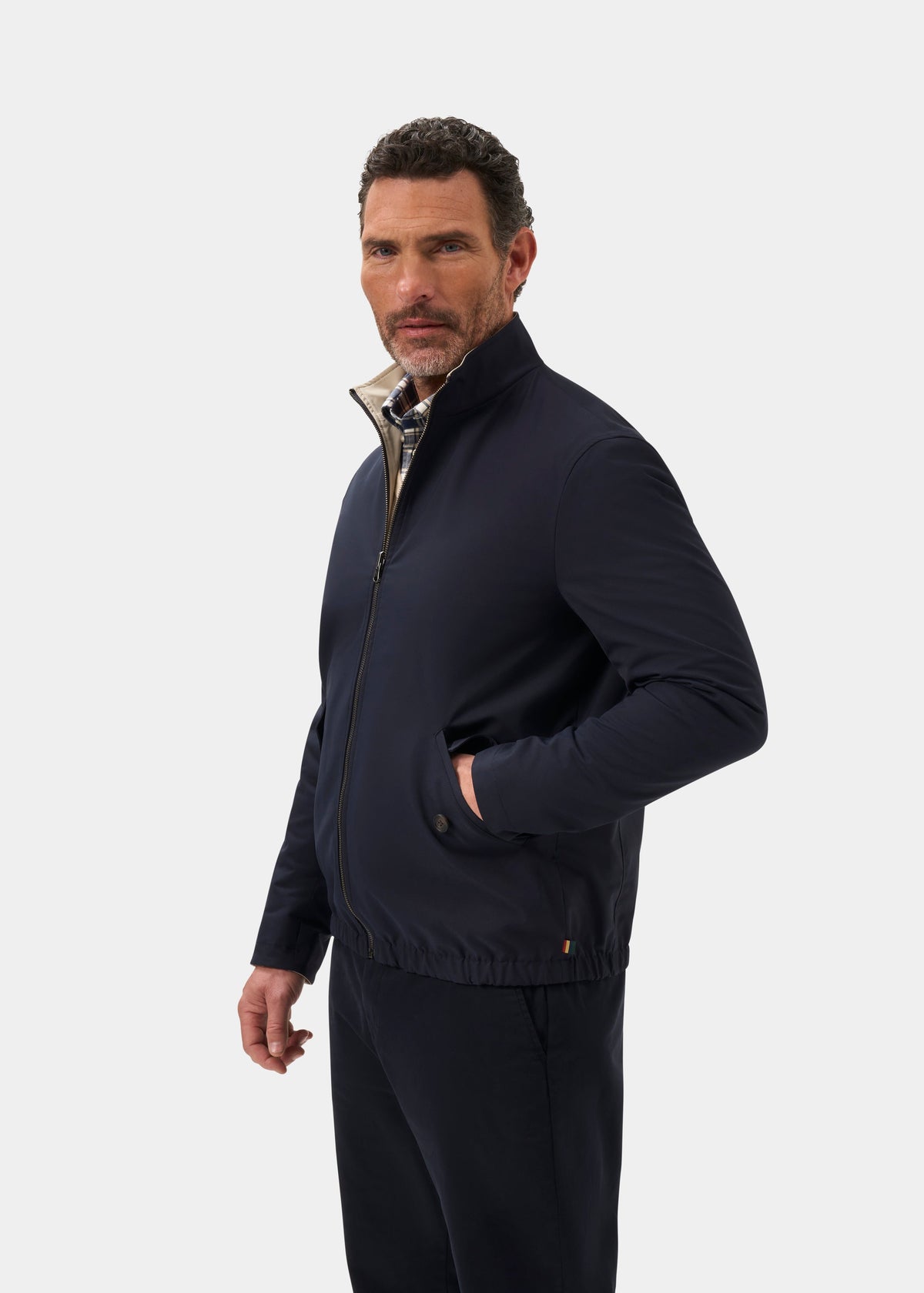Man wearing Lakeward Men’s Reversible Bomber Jacket in Navy and Beige stands with one hand in his pocket, facing camera.