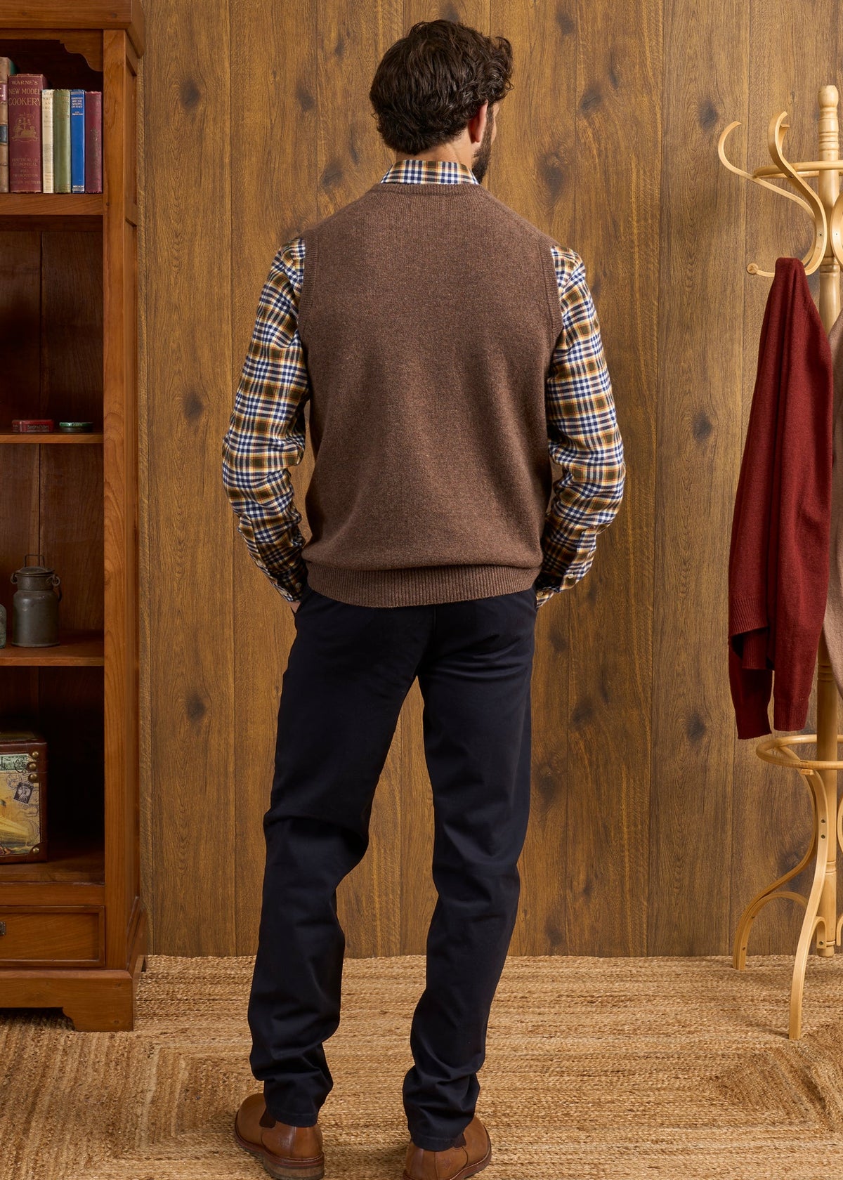 A man seen from behind wearing a tobacco Norfolk Lambswool V-Neck Slipover In Tobacco over a plaid shirt and dark trousers.