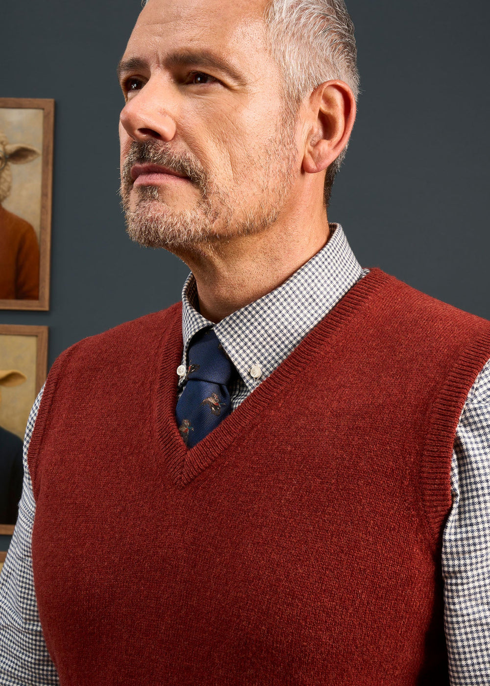 A man wearing a Norfolk Lambswool V-Neck Slipover In Sienna over a patterned dress shirt and dark tie.