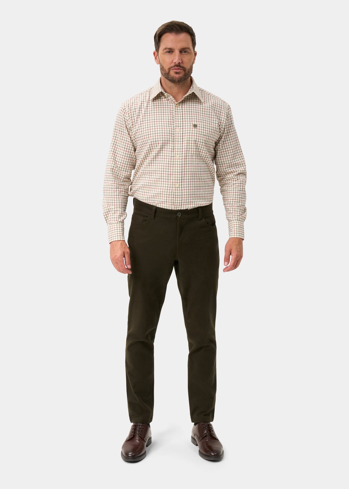 A man modeling a long-sleeve button-down shirt with a beige and brown checkered pattern, paired with dark olive trousers and brown leather dress shoes, against a light gray background.
