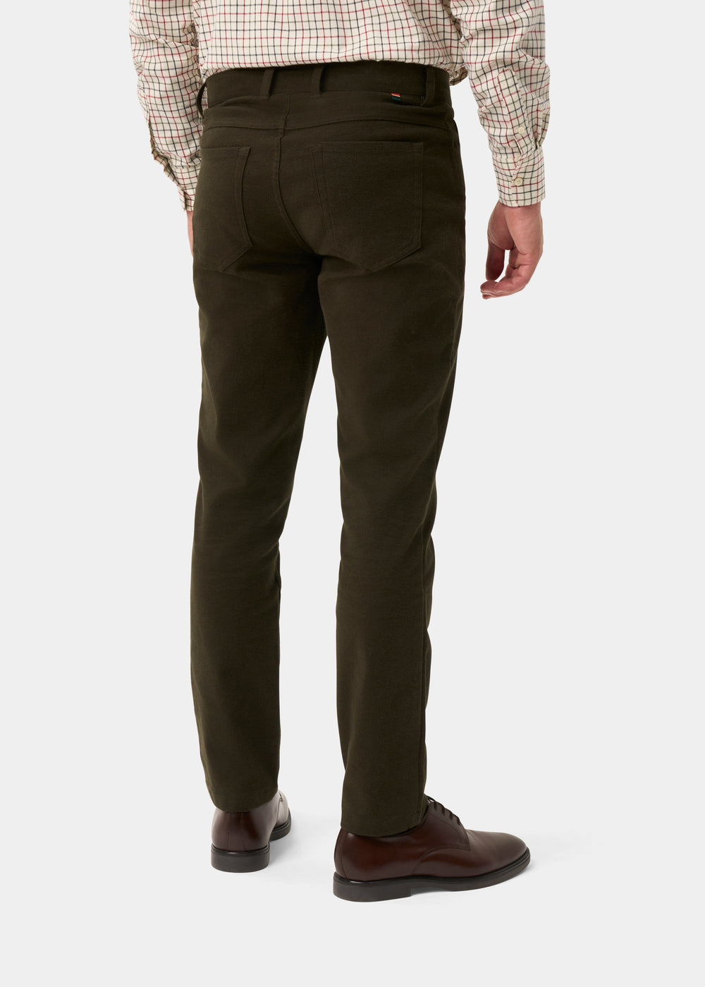 Rear view of a person wearing dark olive green slim-fit trousers, a beige and red checkered shirt, and dark brown leather shoes, against a light gray studio background.