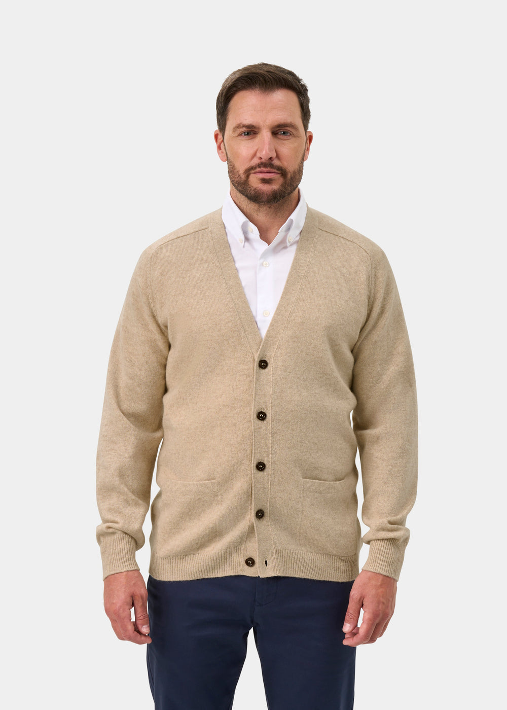 Man in Cornwall Lambswool V-Neck Cardigan in Linen, over a white shirt and navy pants, on a plain white background.