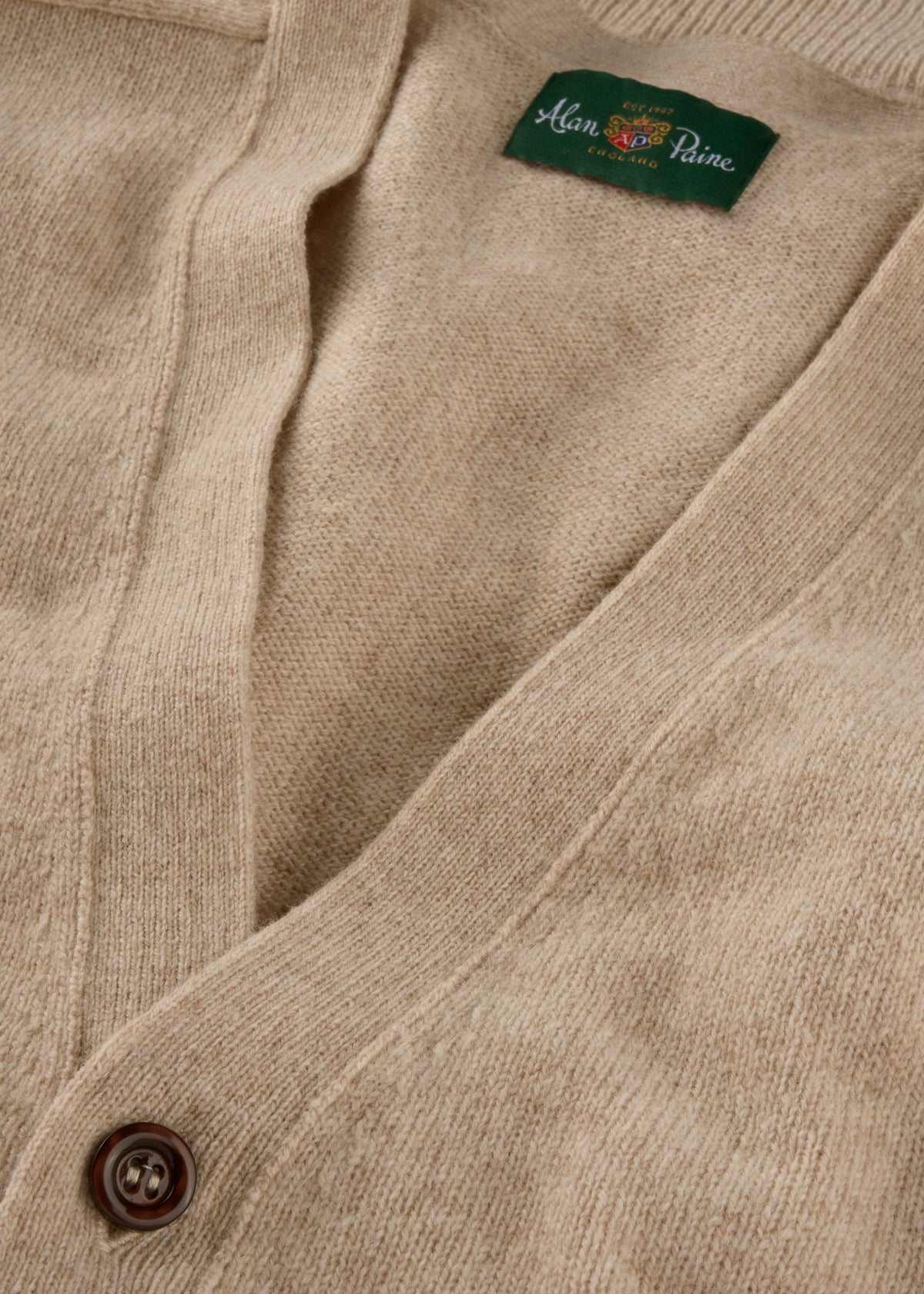 Close-up of the Cornwall Lambswool V-Neck Cardigan in Linen, Classic Fit, with button and green Alan Paine label.