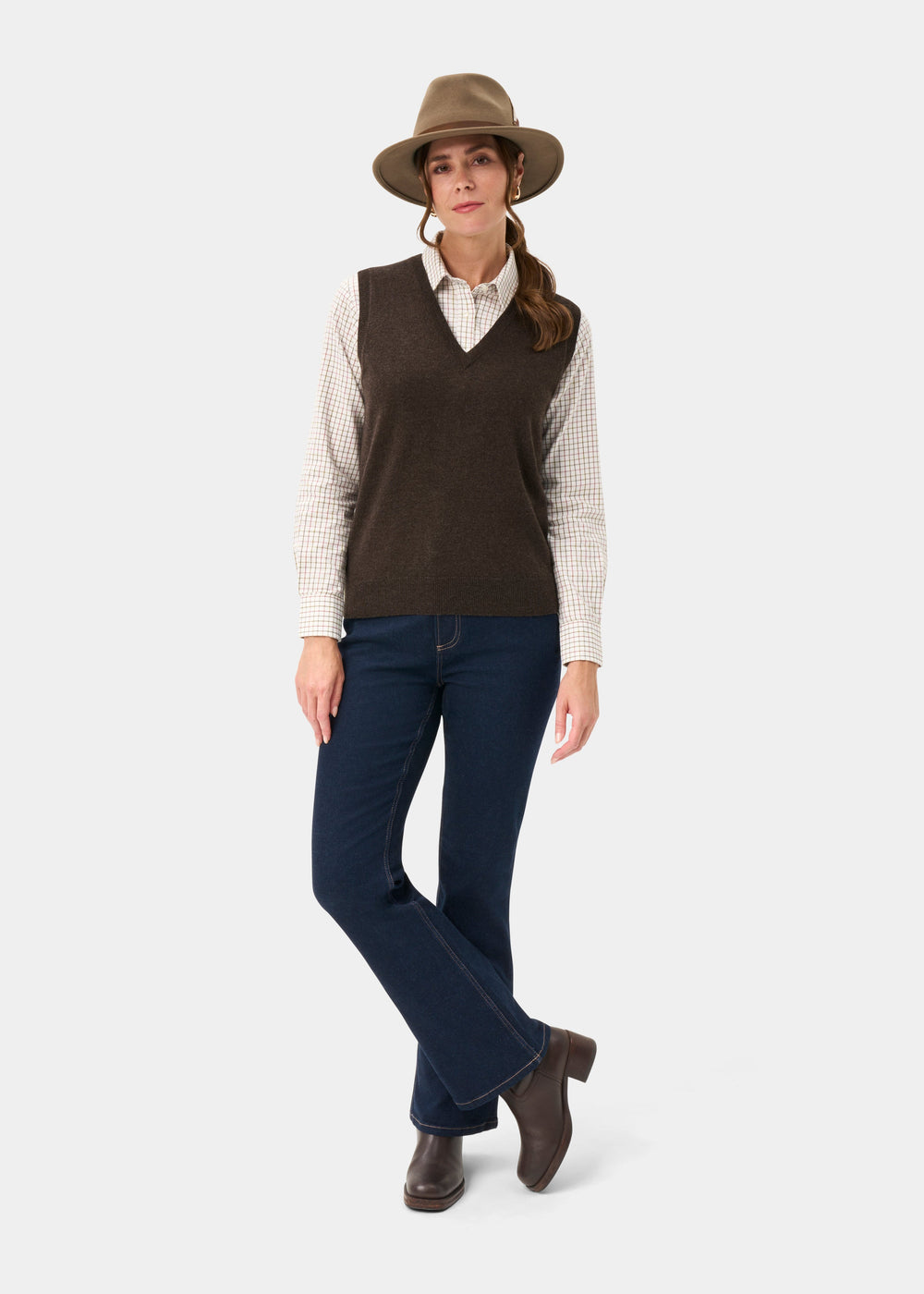 Woman in Erin Wool & Cashmere V-Neck Slipover in Walnut, brown hat, plaid shirt, blue jeans, and boots on white background.