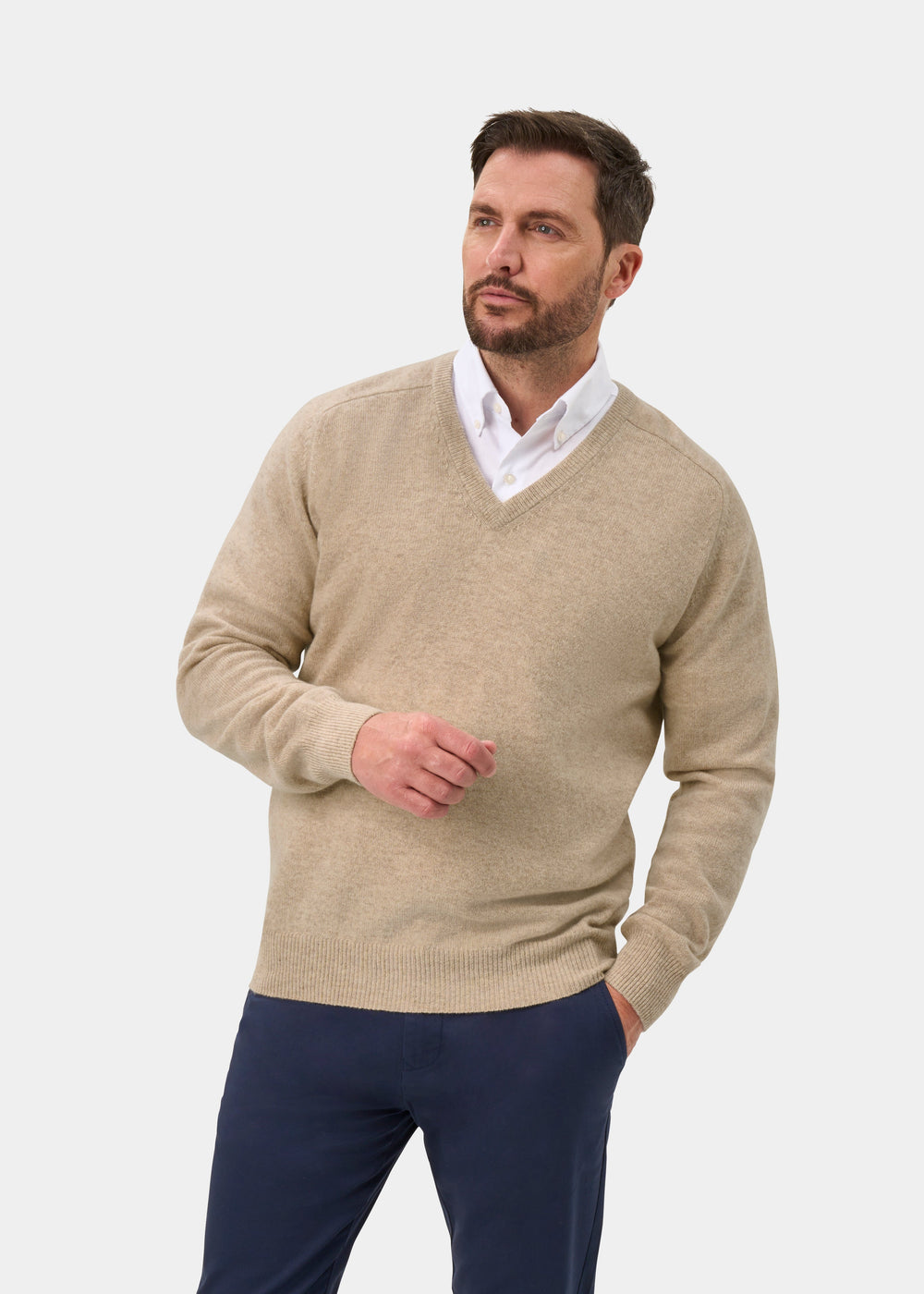 Man wears Hampshire Lambswool V-Neck Jumper In Linen, classic fit, over white shirt; poses against light background.