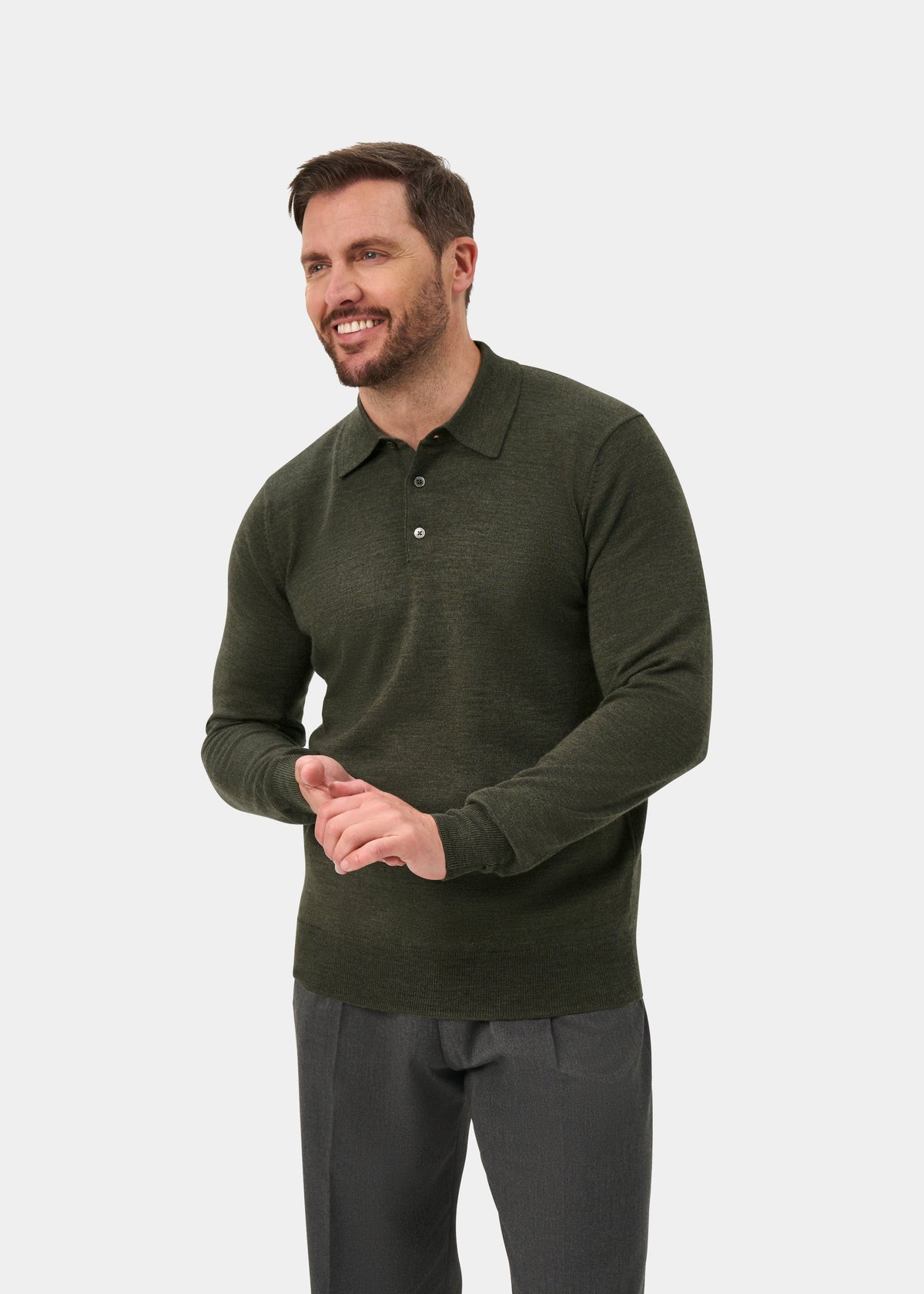 Man in Hindhead Men’s Merino Wool Polo Shirt in Seaweed, regular fit, and gray pants, smiling against plain background.