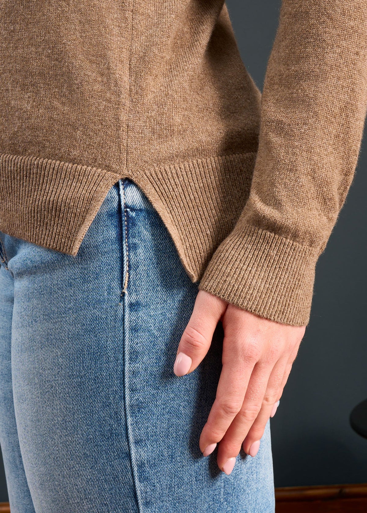 Person in light blue jeans and the Isla Wool & Cashmere V-Neck Jumper in Pecan, standing with hand relaxed at side.