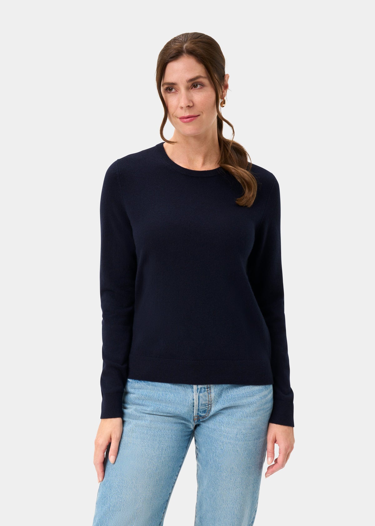 Woman wears Ivy Wool & Cashmere Crew Neck Jumper in Dark Navy with light blue jeans against white background, looking aside.