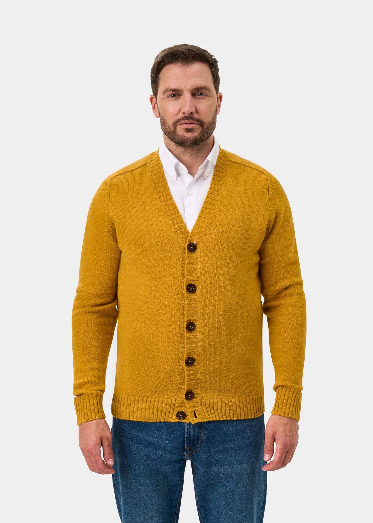 Man wearing Kinloch Supersoft Shetland Wool V-Neck Cardigan in Old Gold over a white shirt and blue jeans.