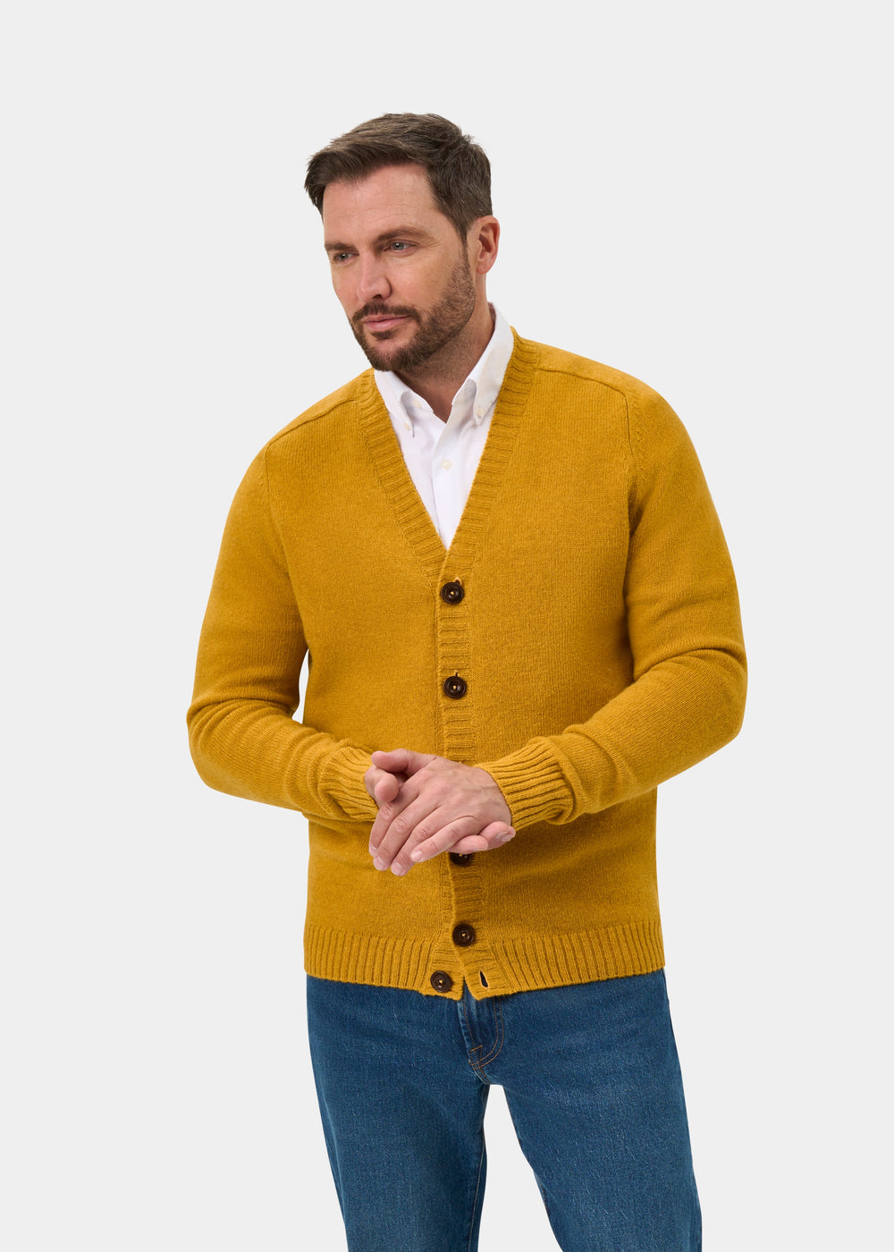 Man in Kinloch Supersoft Shetland Wool Cardigan in Old Gold and white shirt stands against a plain white background.