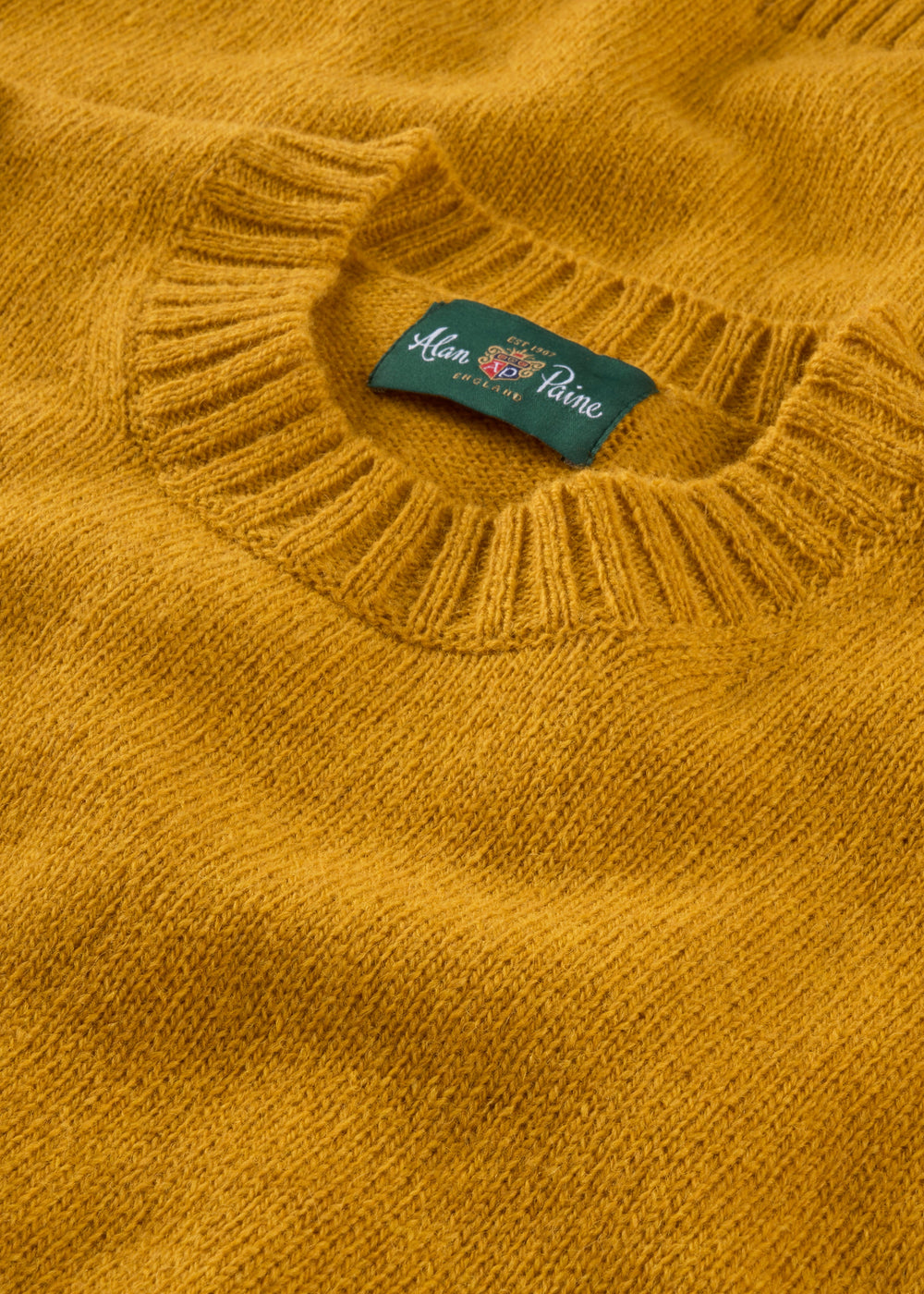 Close-up of the Kinnadie Supersoft Shetland Wool Crew Neck Jumper in Old Gold, regular fit, green label at collar.