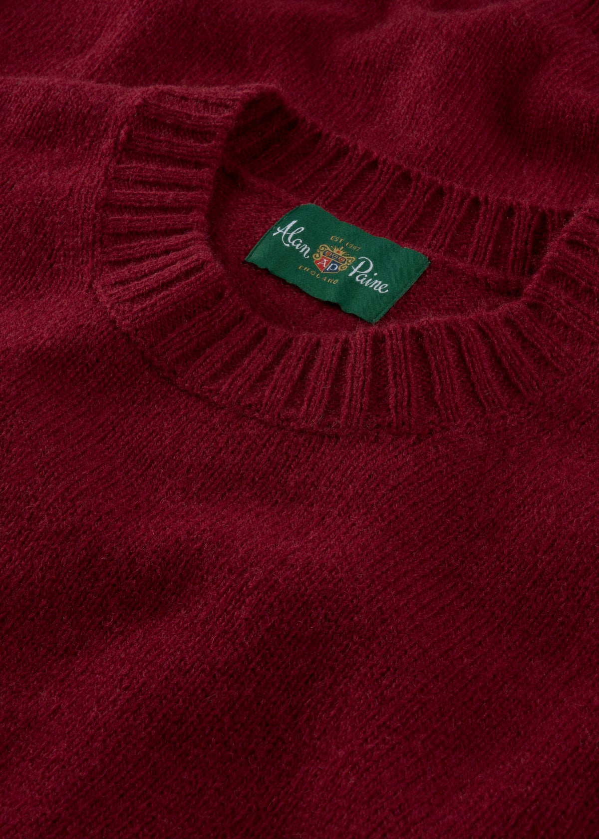 A close-up of a Kinnadie Supersoft Shetland Wool Crew Neck Jumper in Venetian with a green Alan Paine label.