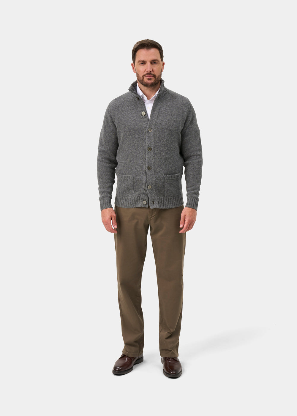 Man in grey mix Landford lambswool mock neck jumper, white shirt, khaki pants, and brown shoes stands by white backdrop.