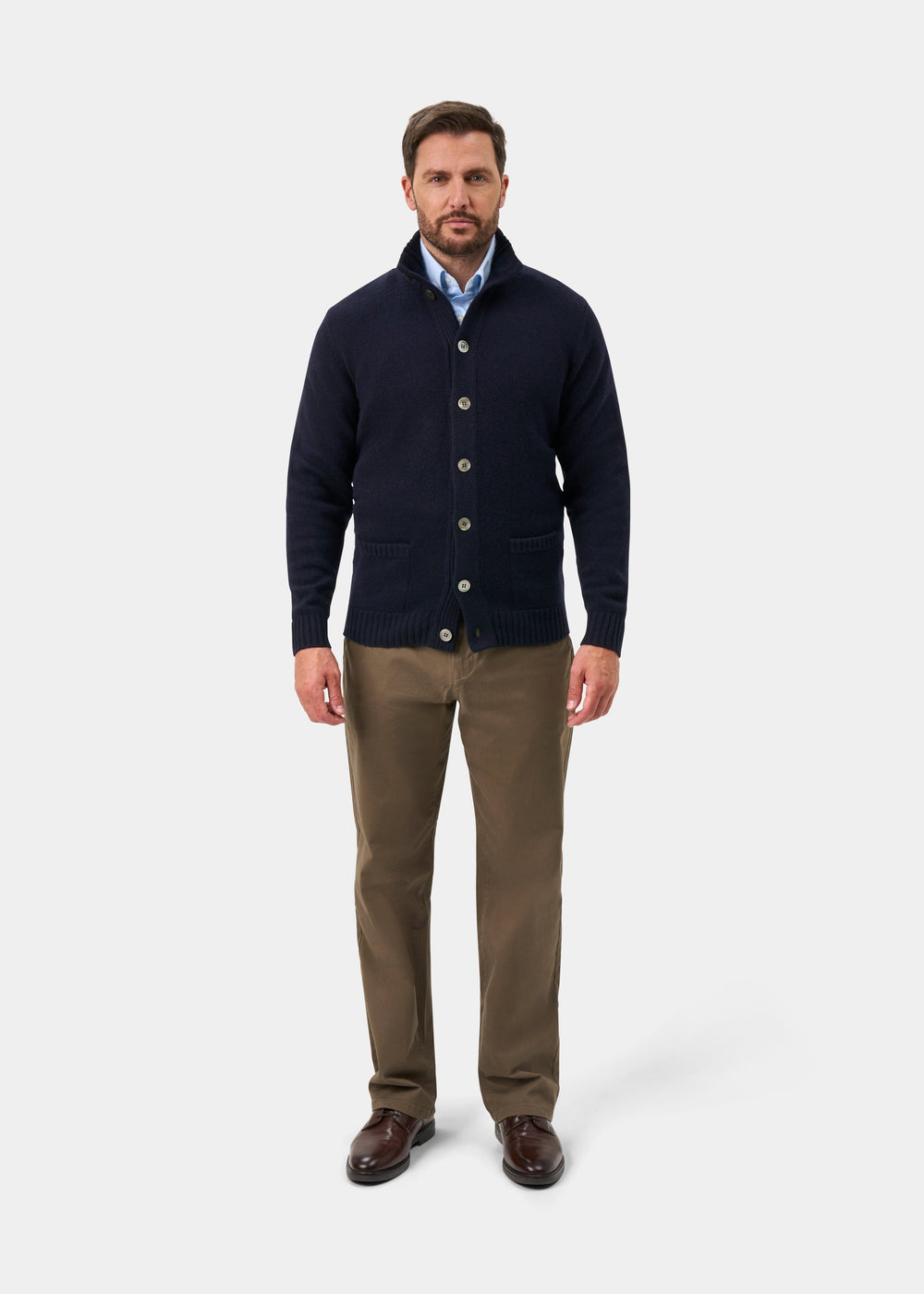 Man in Landford Lambswool Buttoned Mock Neck Jumper in Navy, blue shirt, khaki pants, brown shoes stands facing forward.