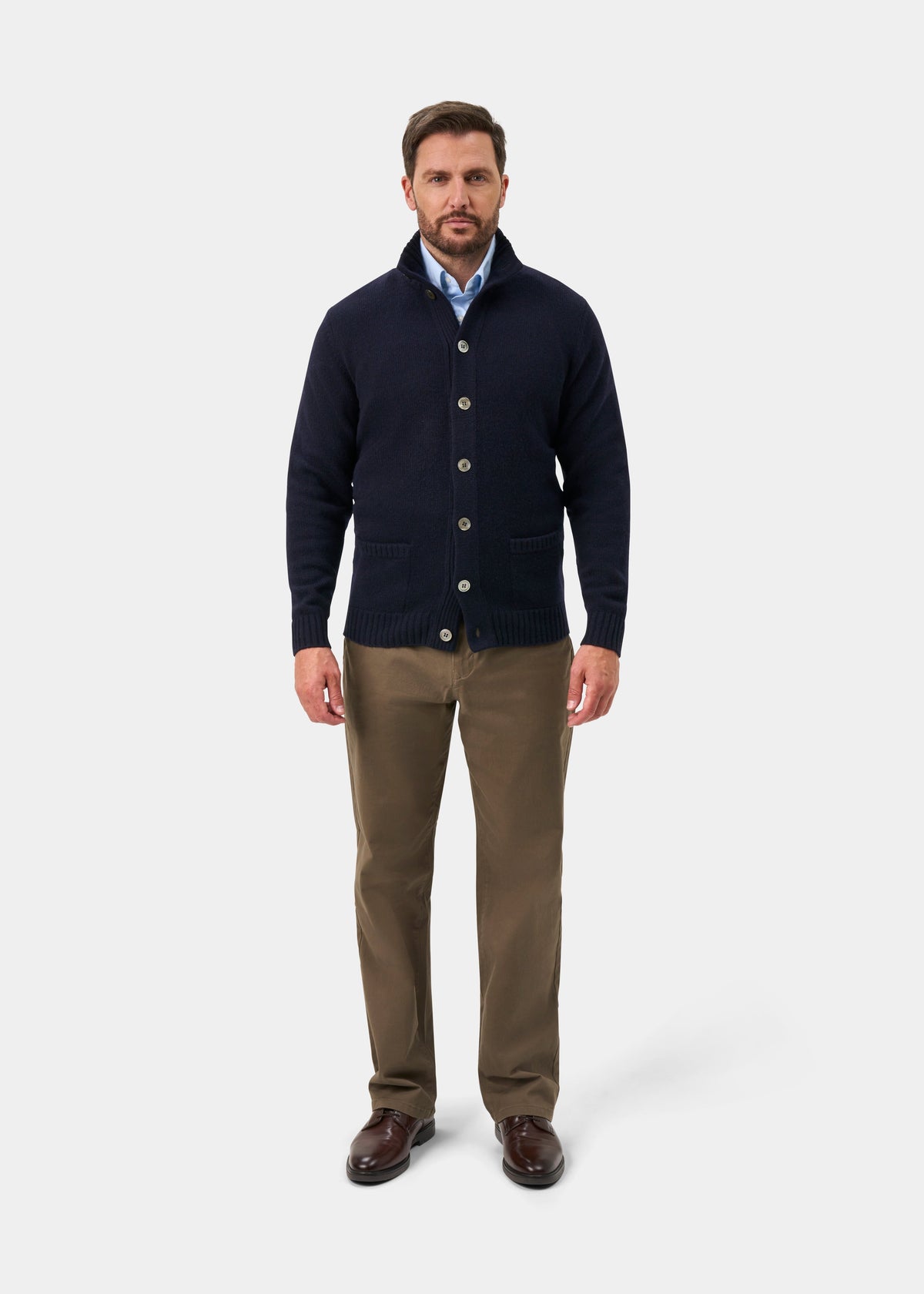 Man in Landford Lambswool Buttoned Mock Neck Jumper in Navy, blue shirt, khaki pants, brown shoes stands facing forward.