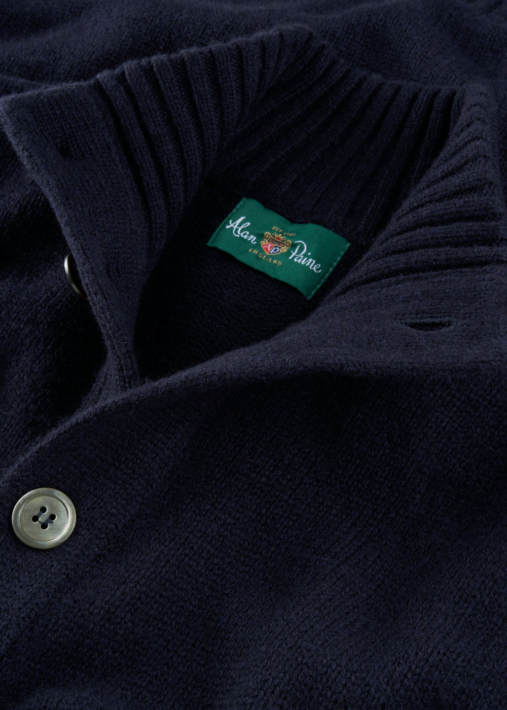 Close-up of the Landford Lambswool Buttoned Mock Neck Jumper in navy with a green Alan Paine collar label.