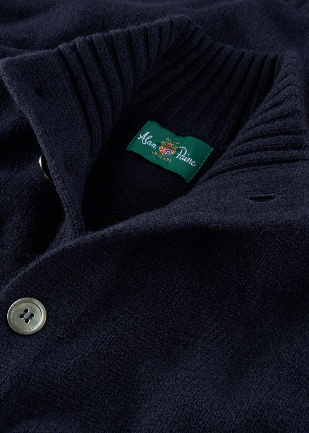 Close-up of the Landford Lambswool Buttoned Mock Neck Jumper in navy with a green Alan Paine collar label.