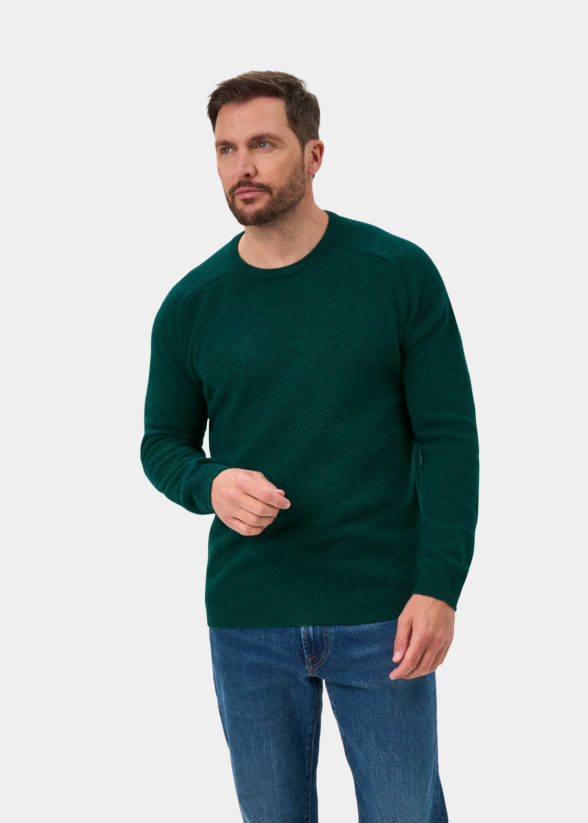 Man in Lenzie Lambswool Crew Neck Jumper in Mallard, Regular Fit, and blue jeans stands against a plain white background.