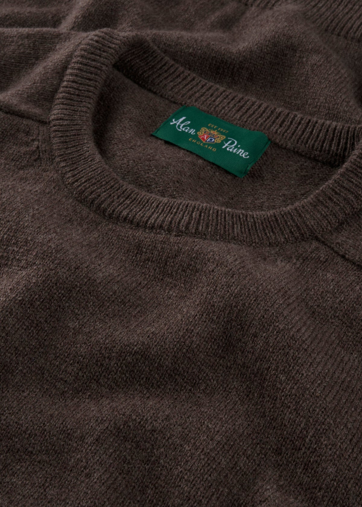 Close-up of the Lenzie Lambswool Crew Neck Jumper in Mocha with a green Alan Paine, England label and fine detailing.