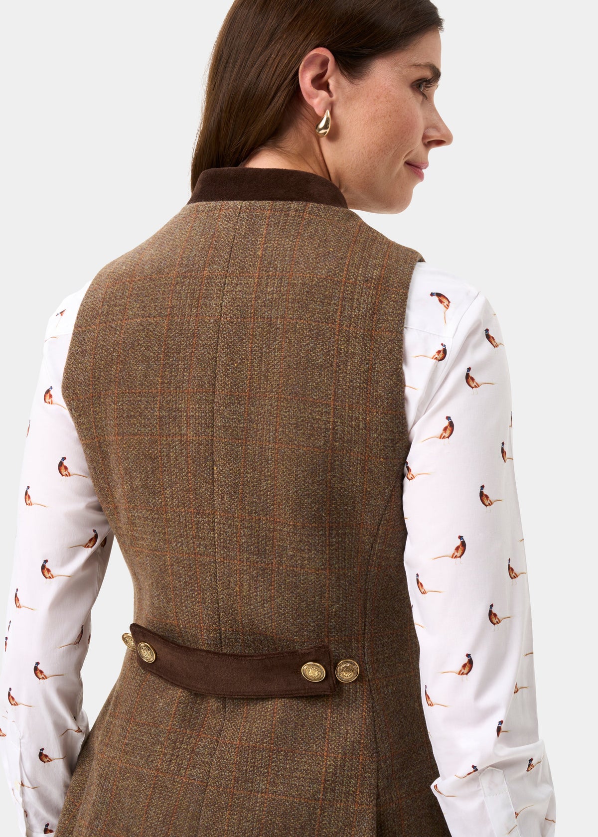 A woman shown from the back wearing a brown tweed vest over a white long-sleeve shirt with a small bird print, against a light gray studio background.